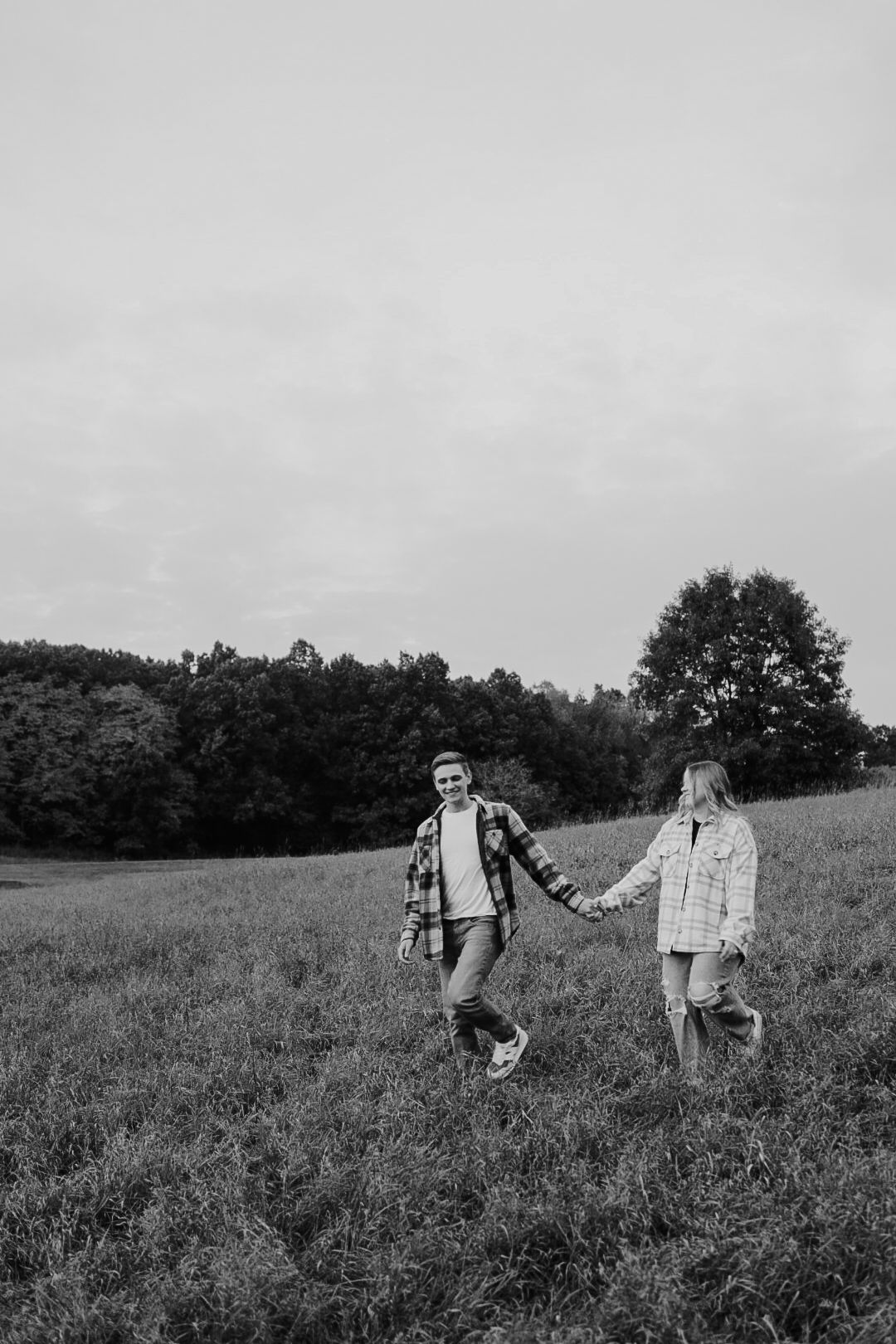 Black and white photo of two people walking through a meadow holding hands.
