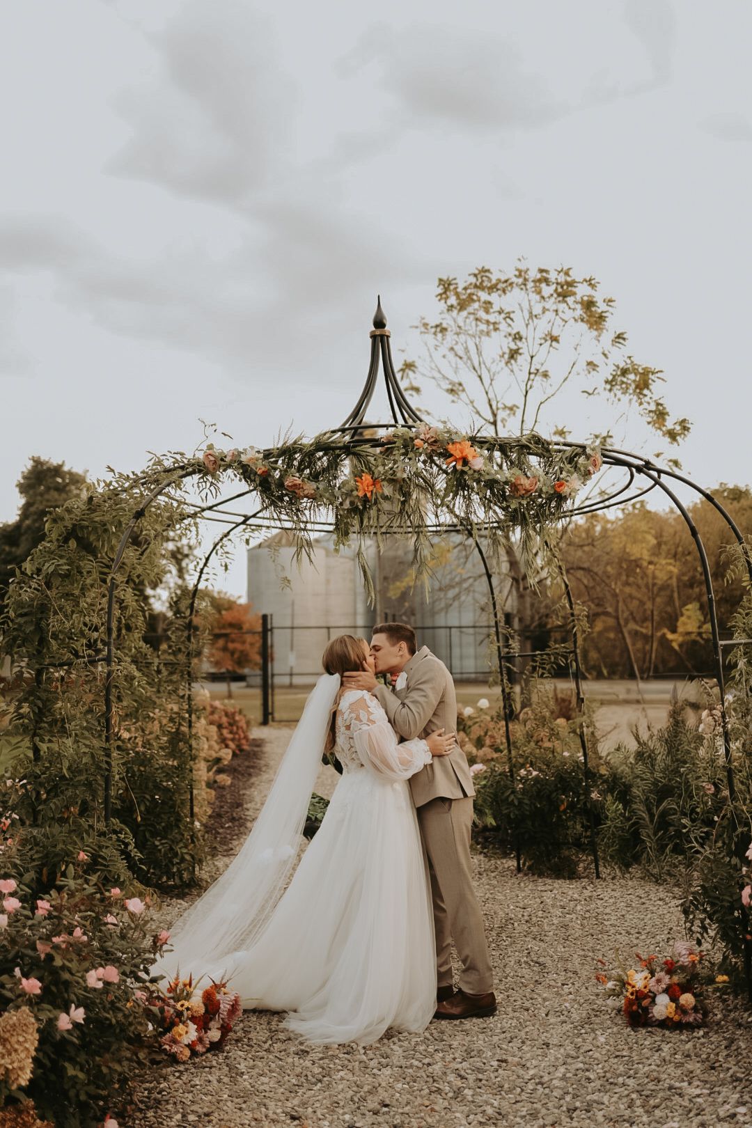 Elegant outdoor wedding ceremony with floral arch and autumn decor on a gravel path.