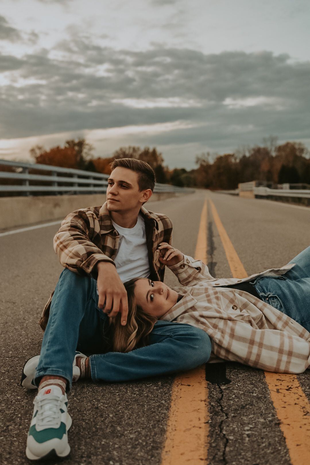 Couple in casual wear resting on yellow road lines during golden hour.