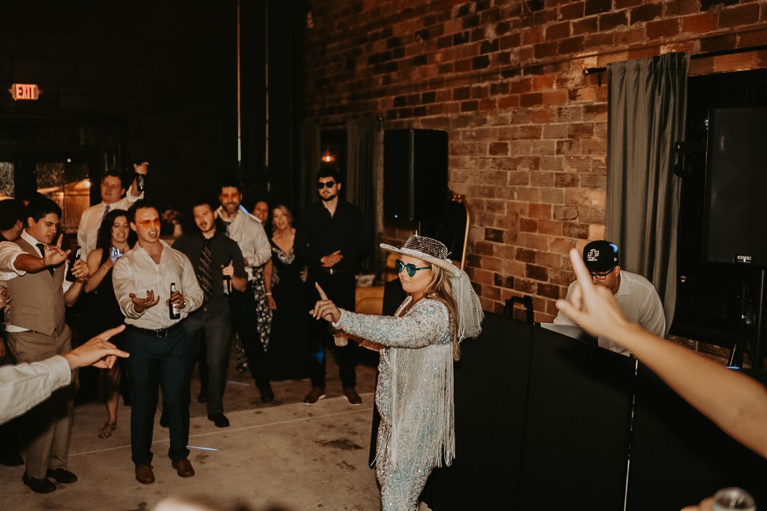 Wedding guests dancing and celebrating in an elegant brick-walled venue.