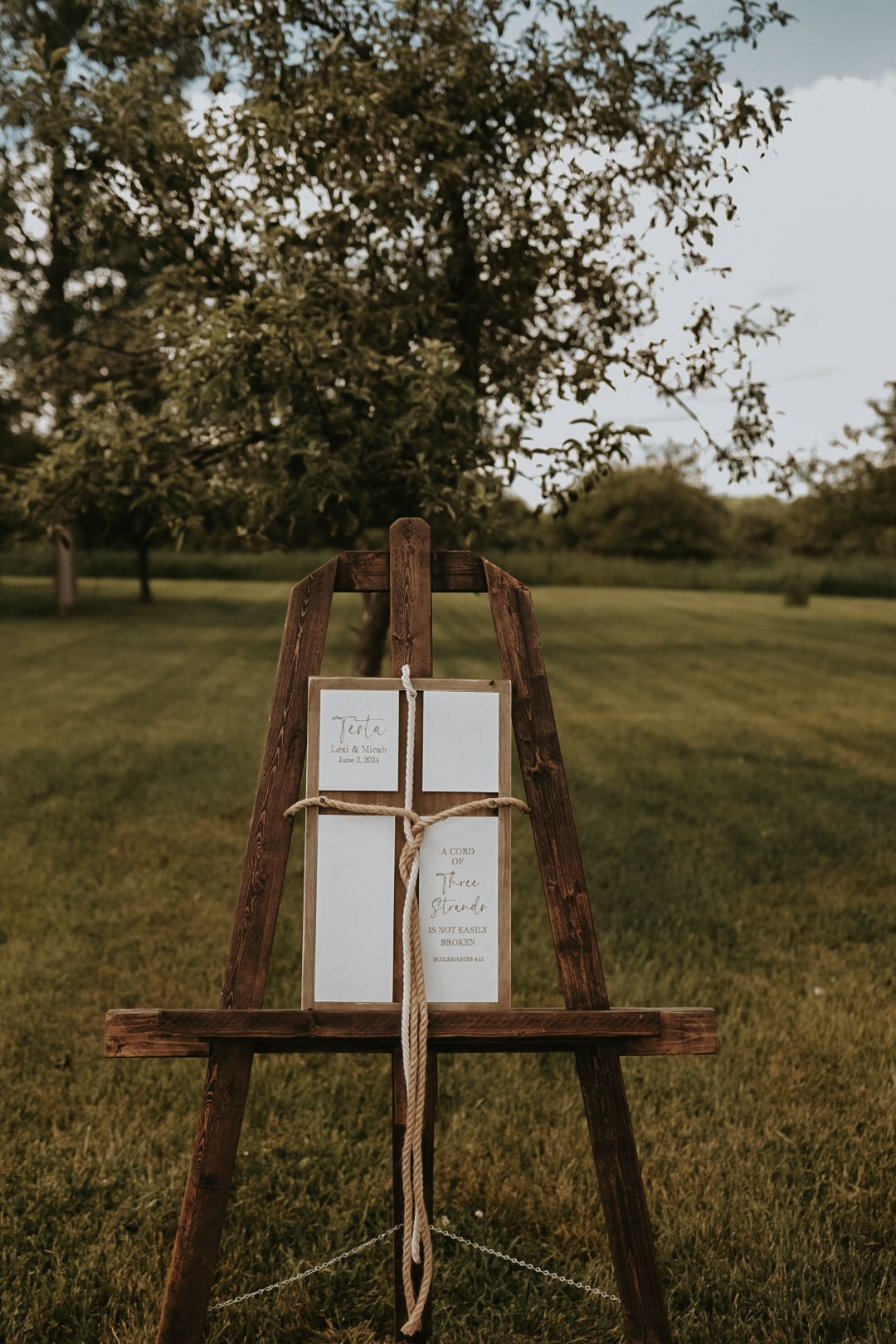 Rustic wooden easel displays wedding signage in an outdoor garden setting.