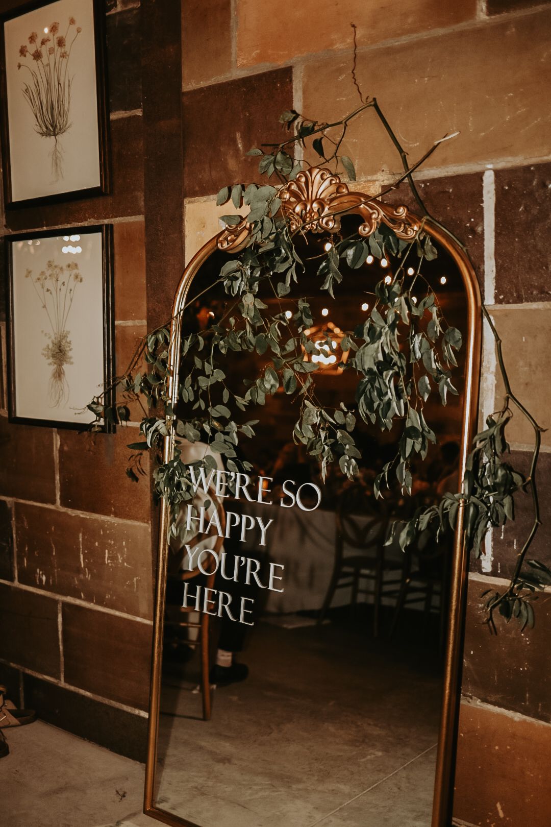 Decorative wedding arch with greenery and illuminated signs reading 'You're Here' and 'Happy'.