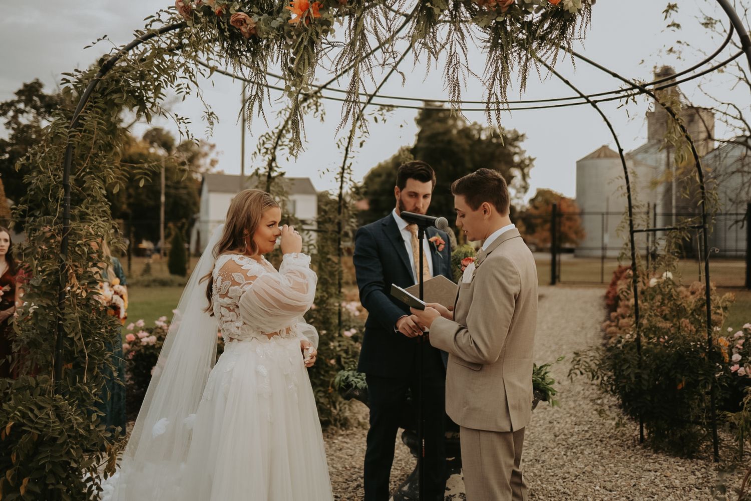 Wedding ceremony under a rustic floral arch with autumn foliage and decorative elements.