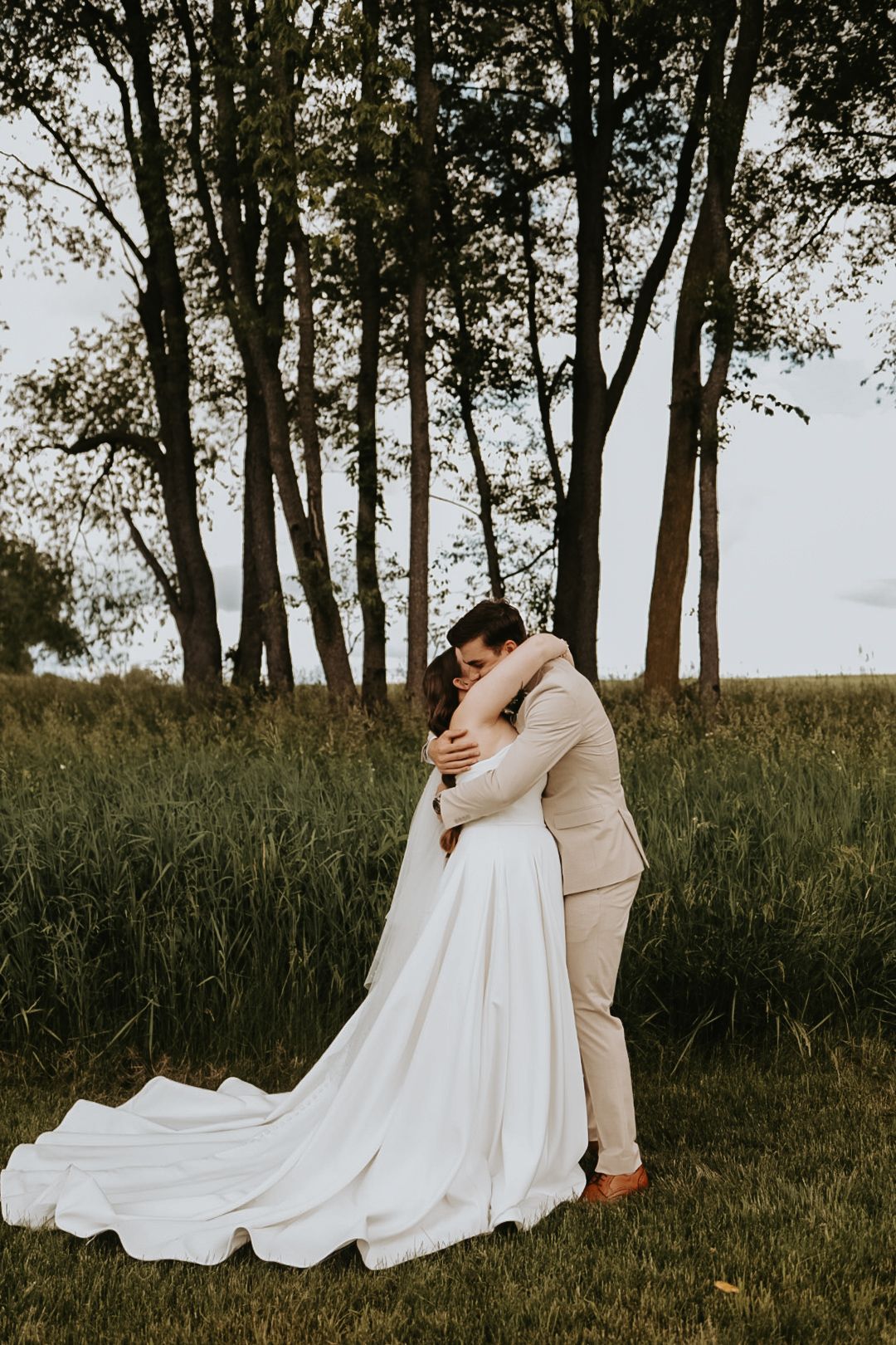 Couple embraces in a romantic moment on their wedding day surrounded by tall trees.