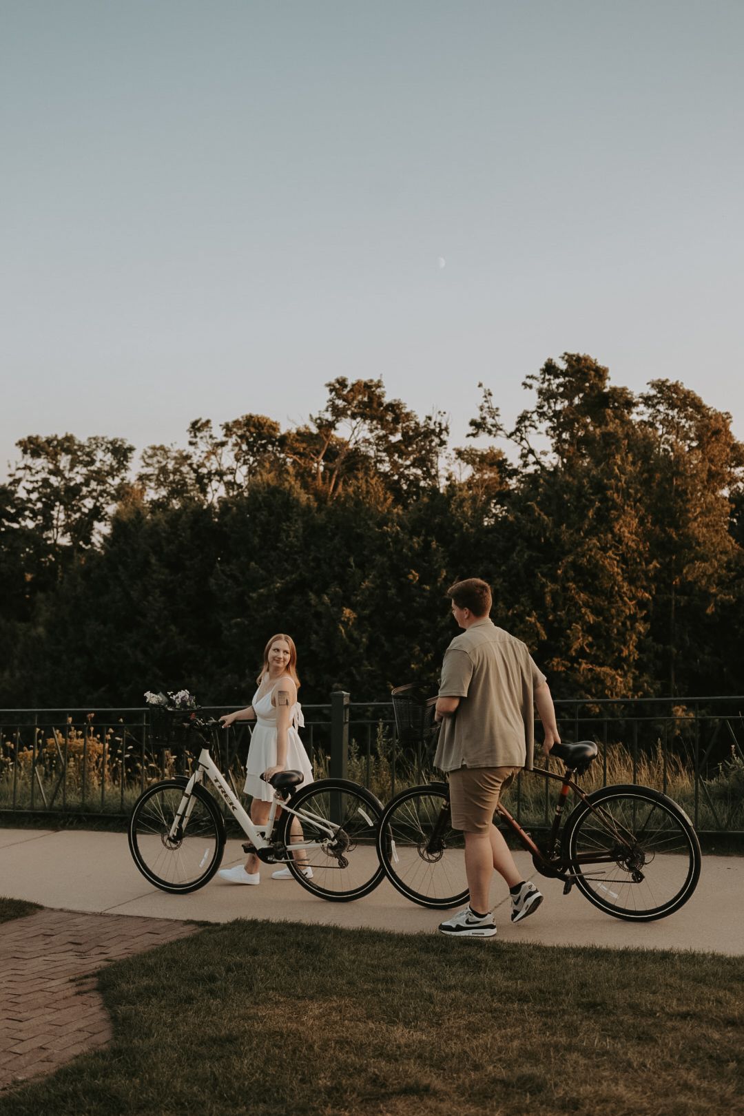 Couple sits with bicycles on path during sunset engagement session.