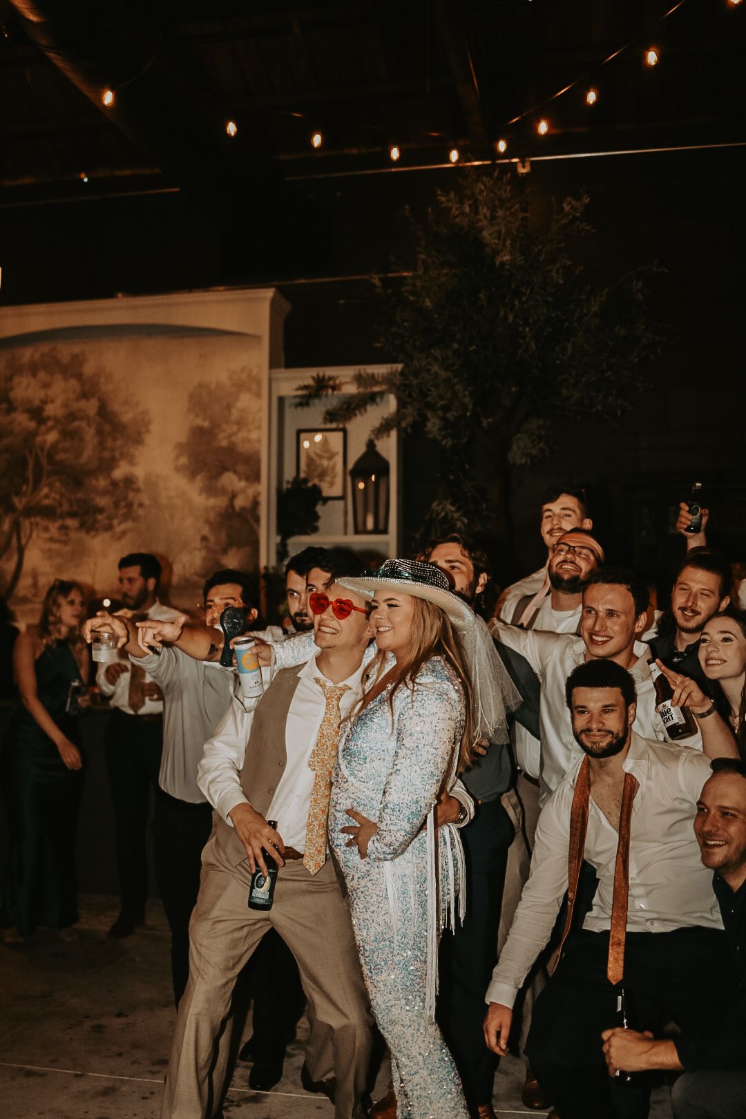 Party crowd dancing and celebrating at night under string lights.