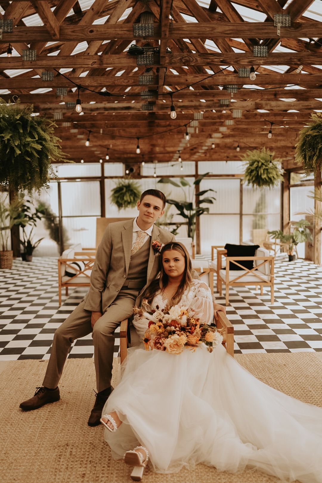 Wedding couple seated in rustic venue with exposed beam ceiling and checkered floor.
