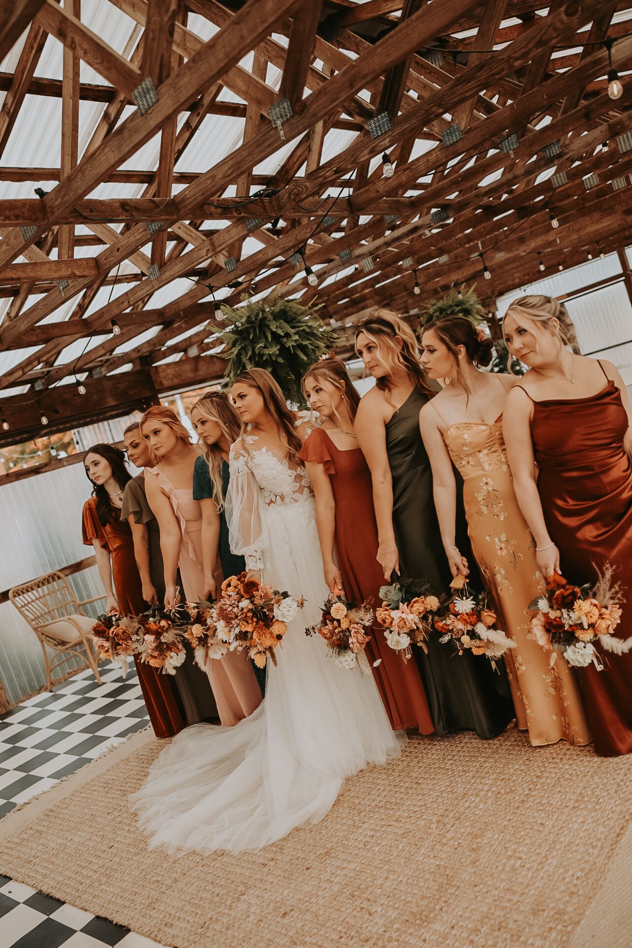 Wedding party poses creatively under wooden beams with burgundy and blush accents.