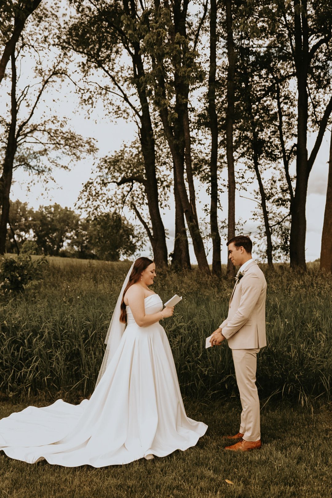 Couple exchanges vows in an outdoor ceremony with tall trees and natural scenery.