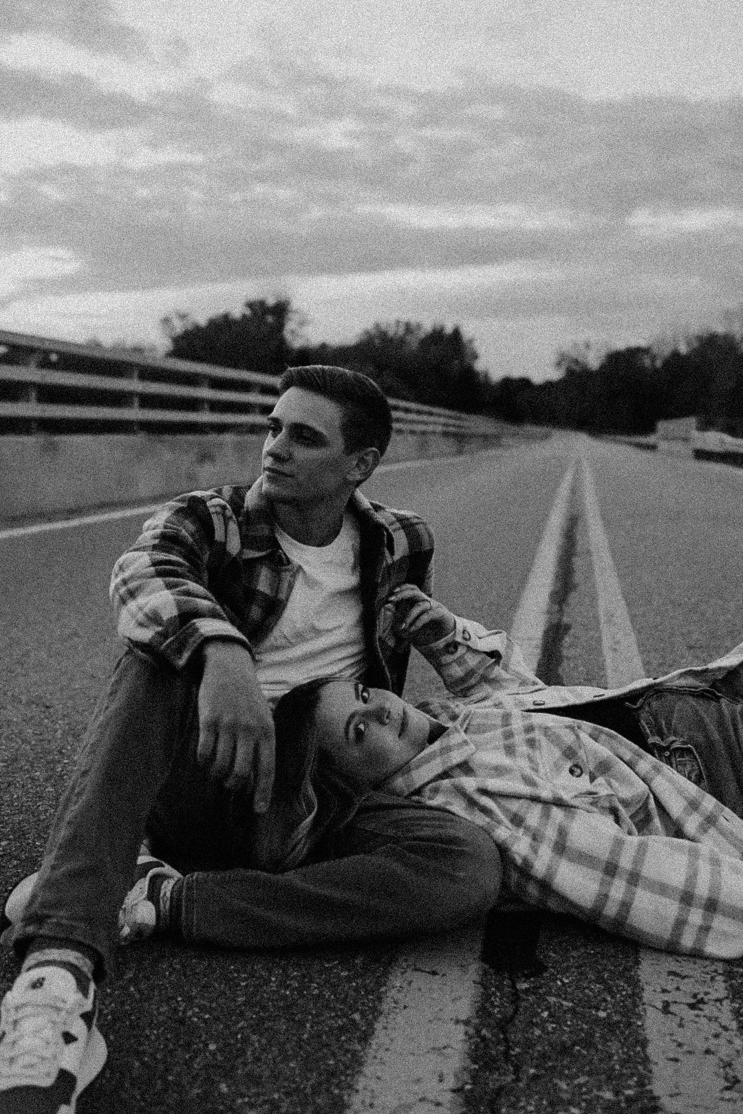 Black and white photo of two people relaxing on empty road at dusk.