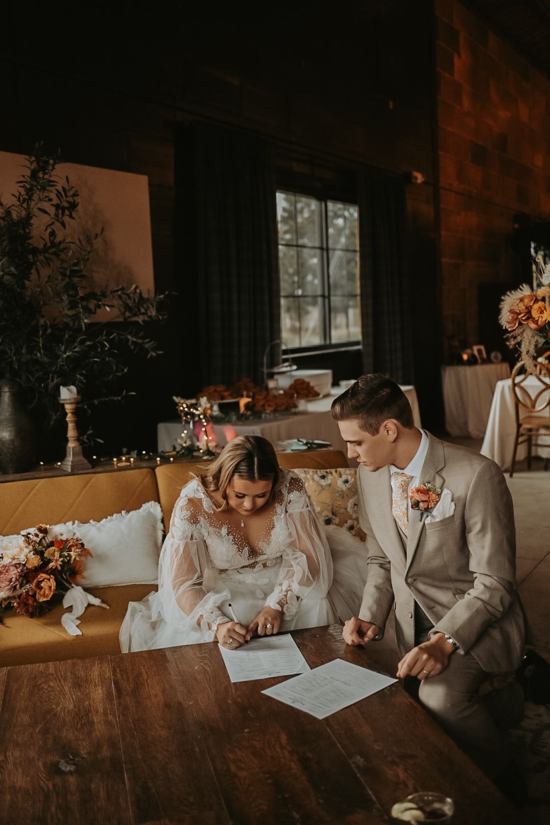 Wedding couple signing documents on vintage furniture in warm indoor lighting.