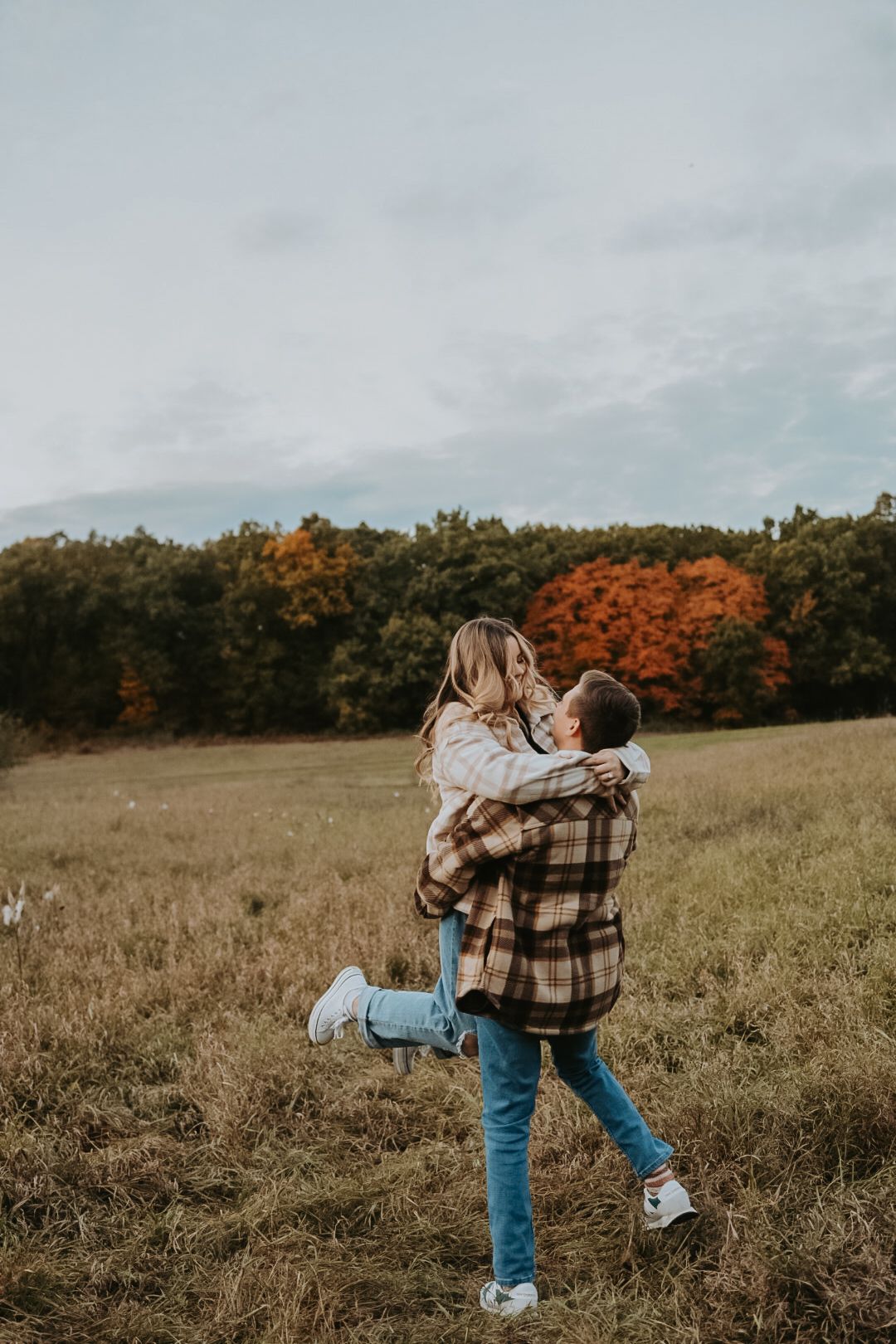 A couple in plaid shirts playfully dances in a golden autumn field.