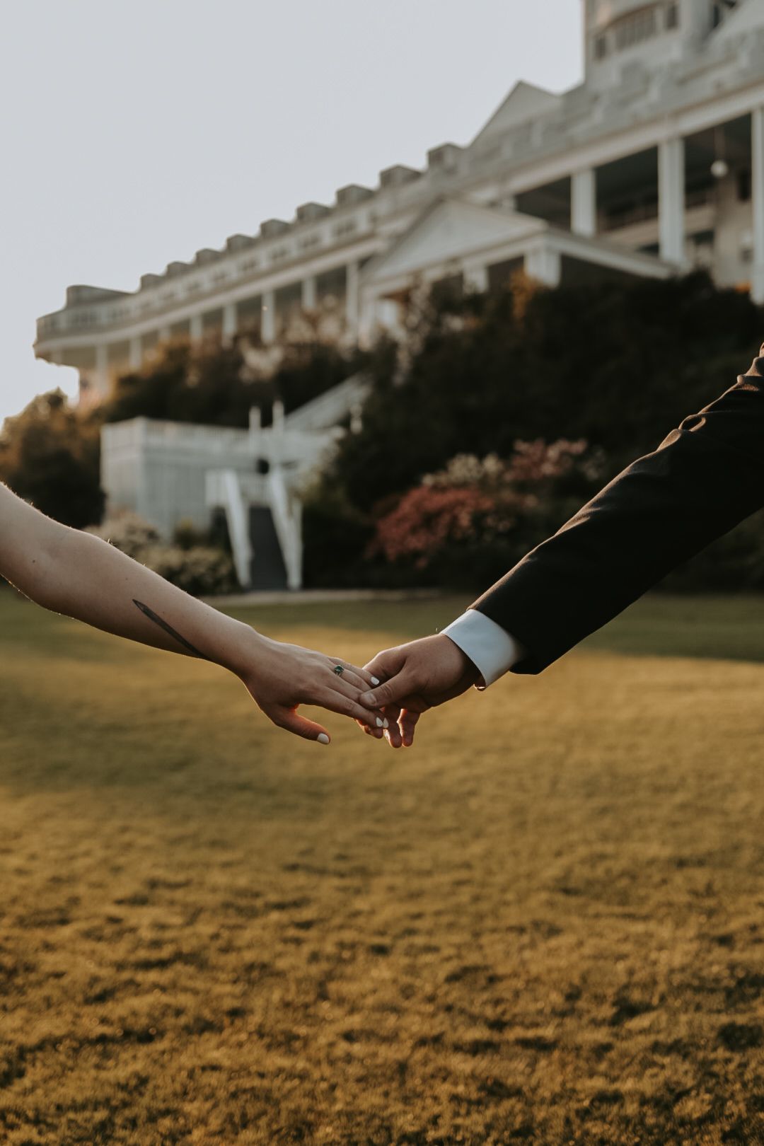 Hands reaching towards each other against a backdrop of a majestic white building at sunset.