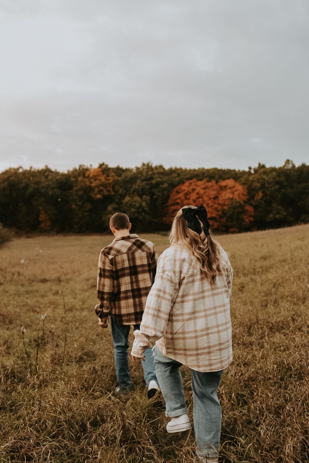 Two people walking through autumn field wearing matching plaid shirts.