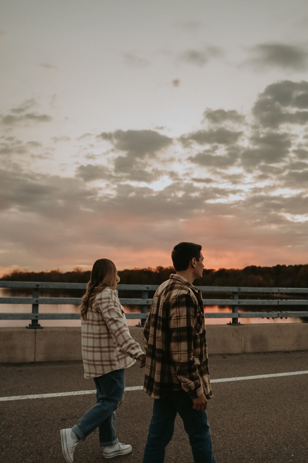 Two people in plaid jackets walking on a bridge during a dramatic sunset.
