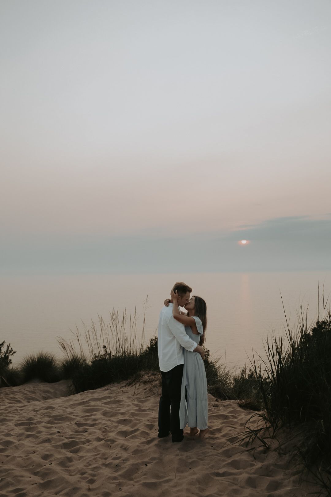 A couple embraces on sandy dunes during a misty sunset.