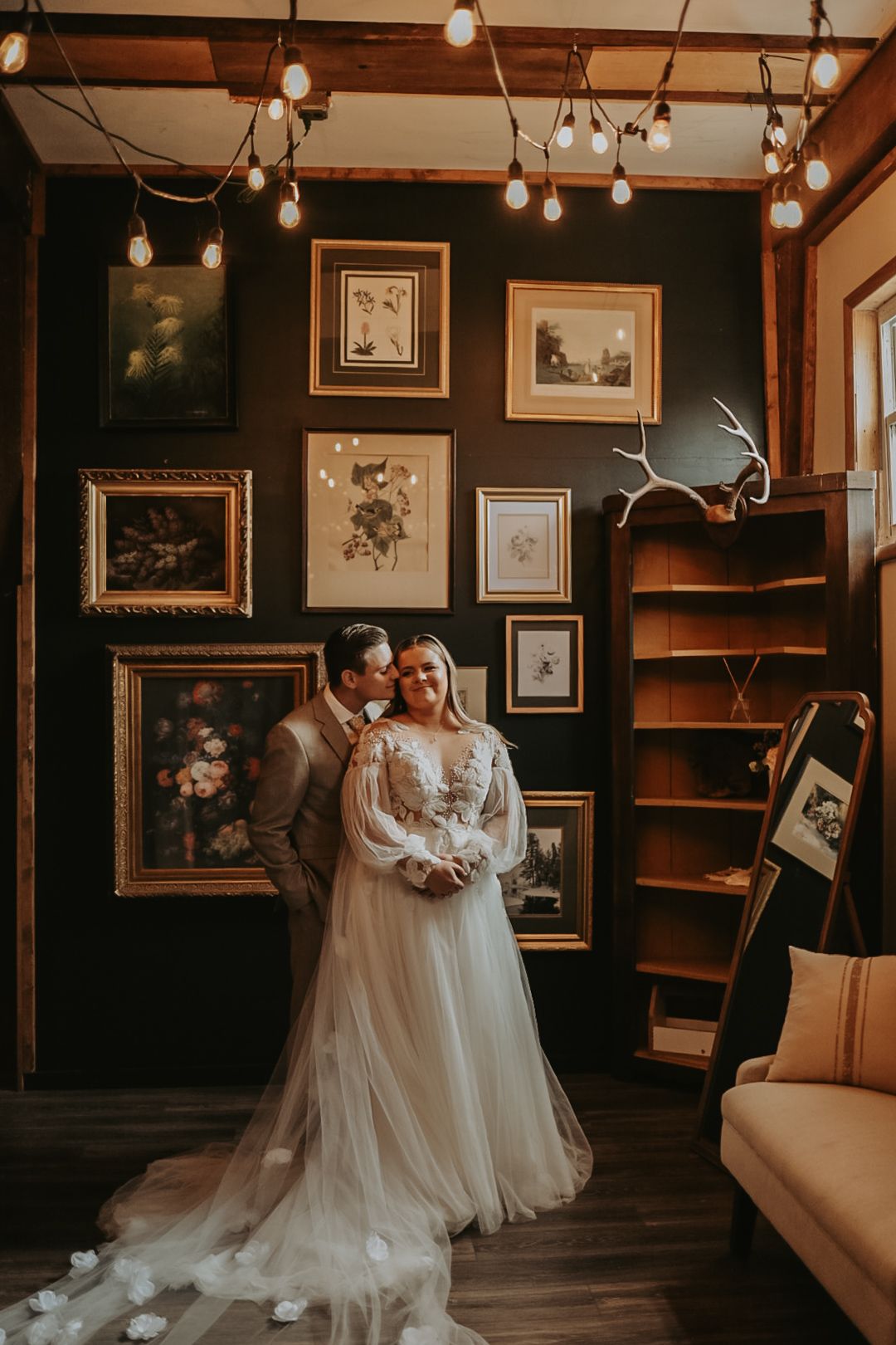 Romantic wedding portrait in vintage-style room with gallery walls and string lights.