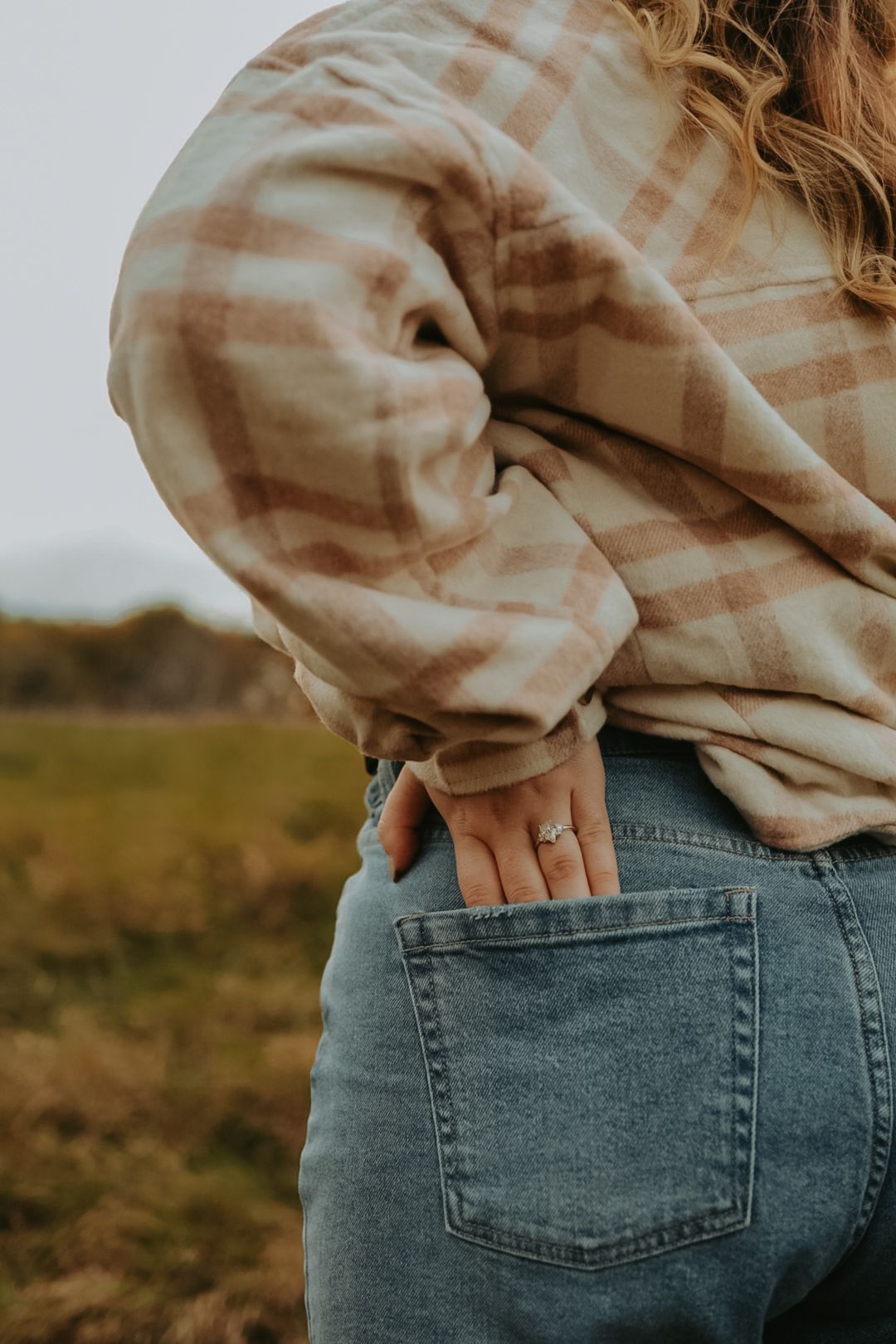 Close-up view of someone wearing a beige plaid shirt and blue jeans with hand in back pocket.