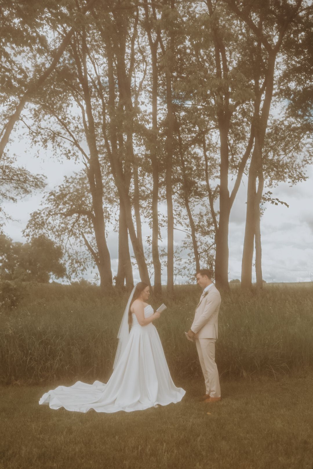 Couple stands together during their outdoor ceremony with sunlit trees creating a natural backdrop.