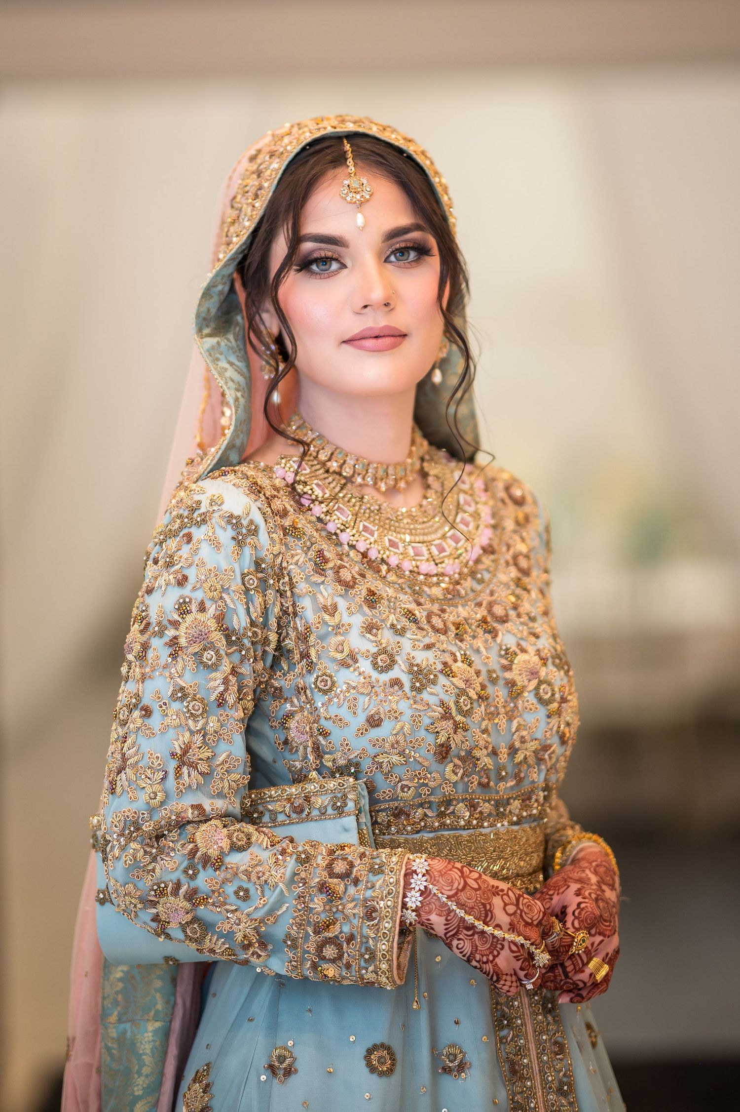 Close-up of bride wearing ornate mint green and gold South Asian wedding attire.