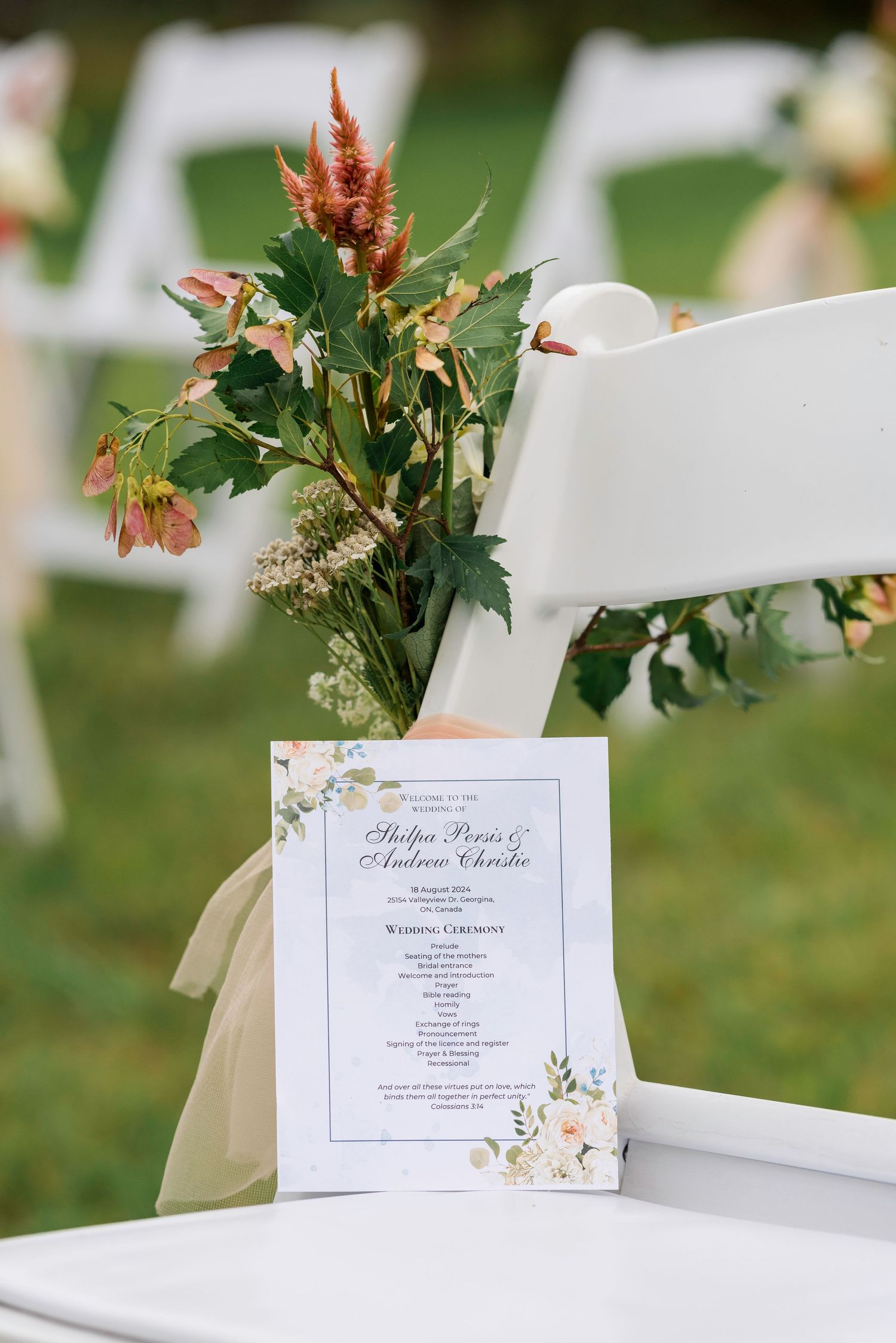 Elegant wedding invitations displayed on white chairs with floral decorations in an outdoor garden setting.