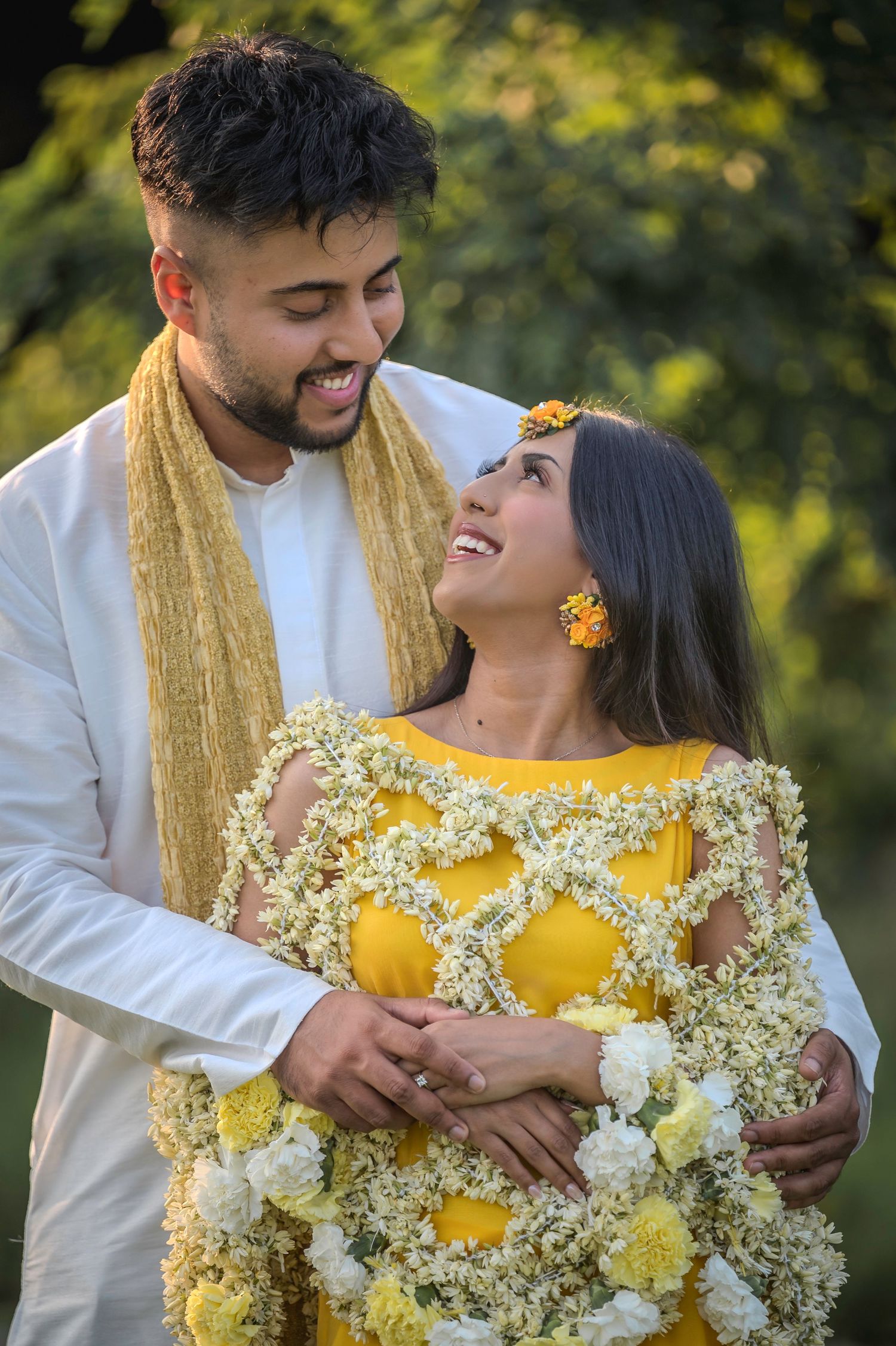 Joyful outdoor portrait featuring yellow floral dress and white traditional attire with gold scarf.