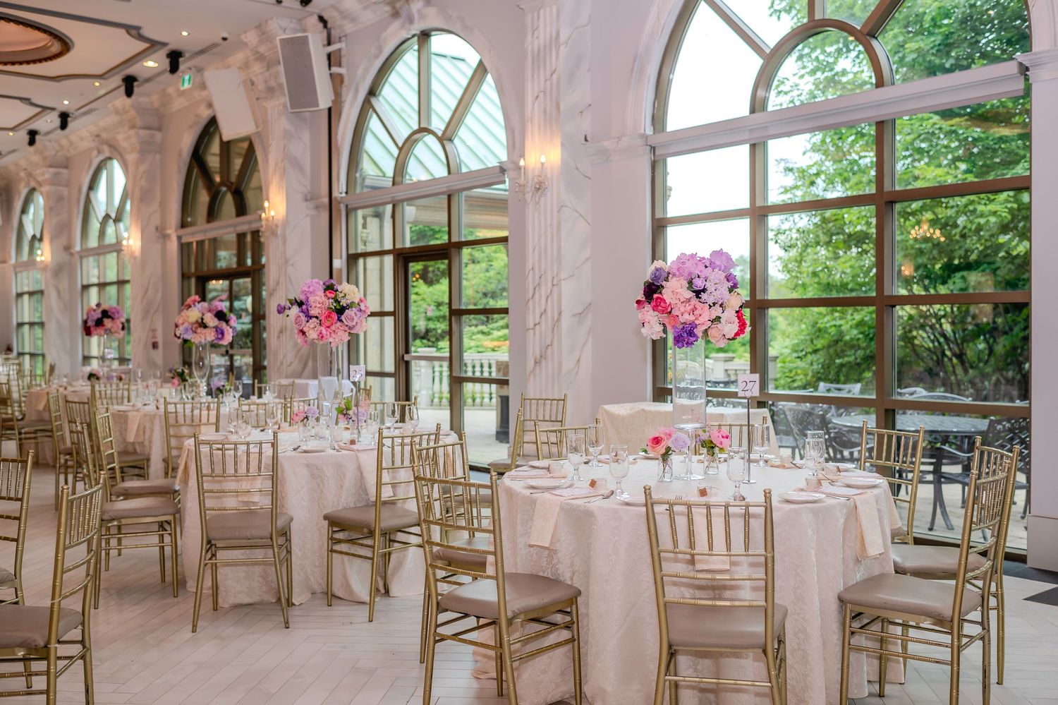 Bright wedding venue with arched windows, white walls, and gold chairs arranged for a ceremony.