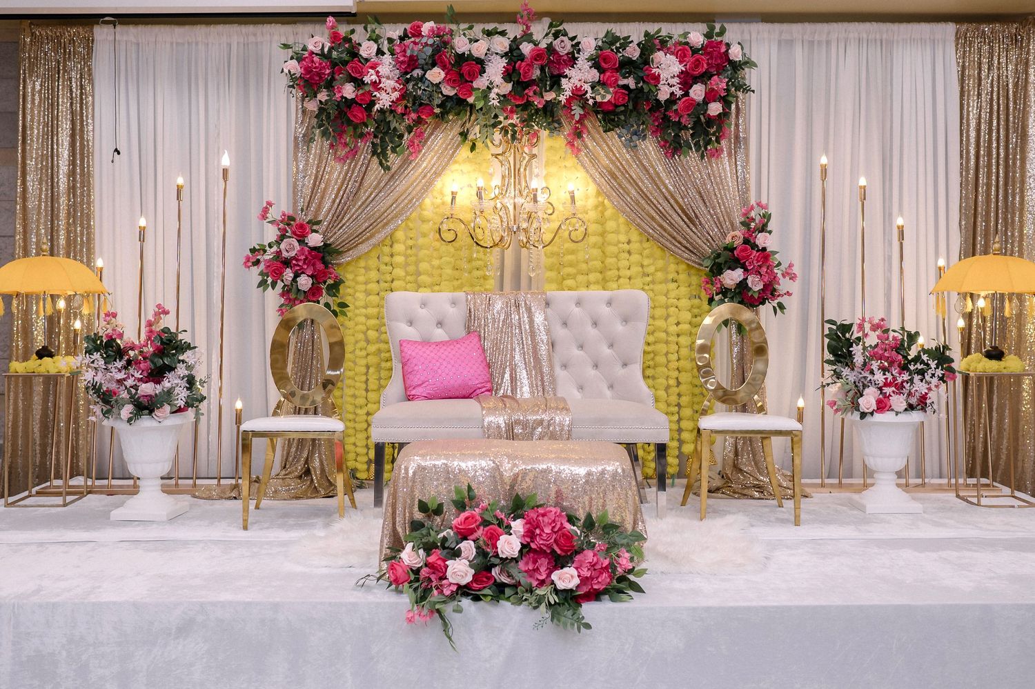 Wedding stage backdrop with pink and red floral arrangements and draped fabric.
