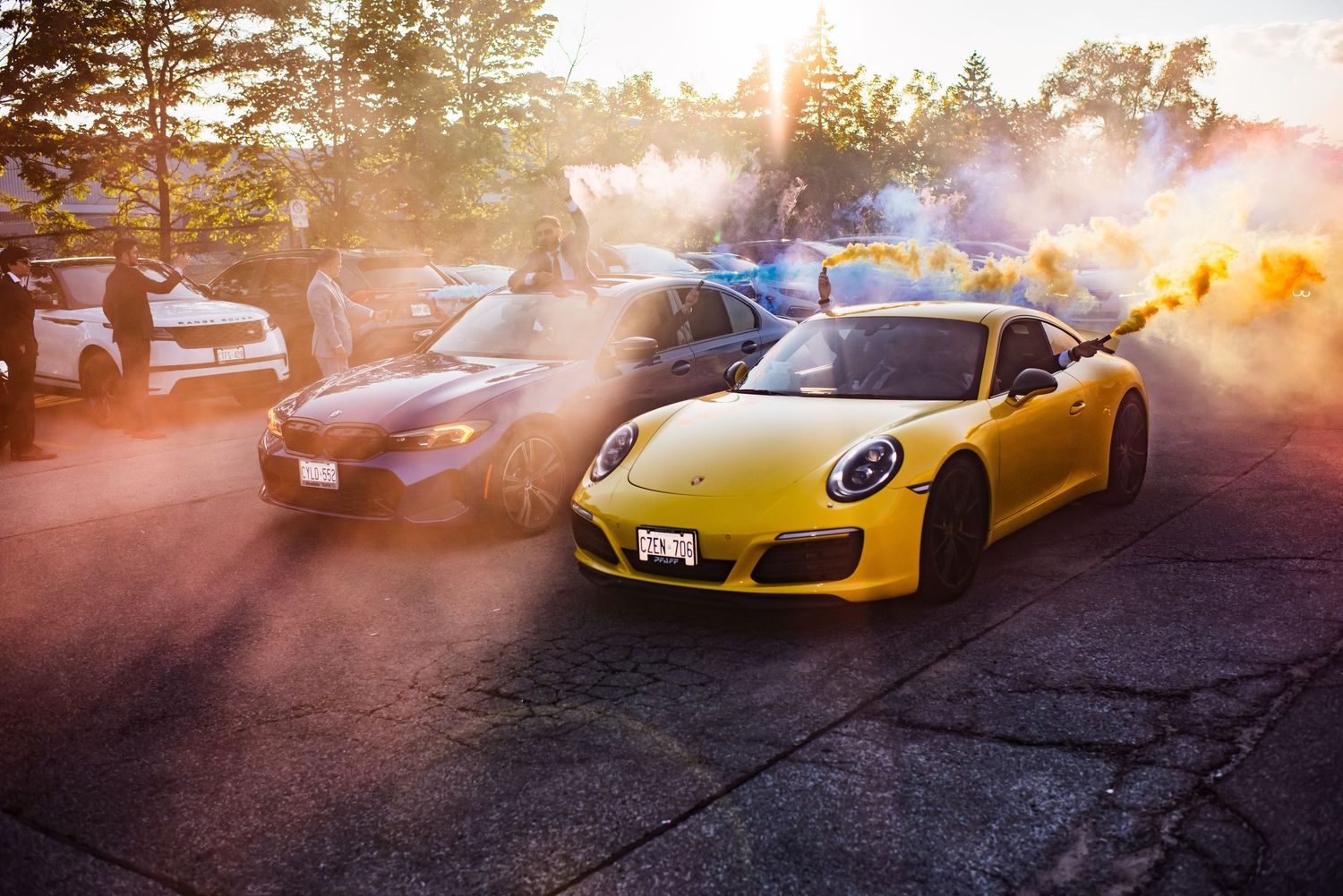 Luxury sports cars lined up at sunset with dramatic lighting and smoke effects.