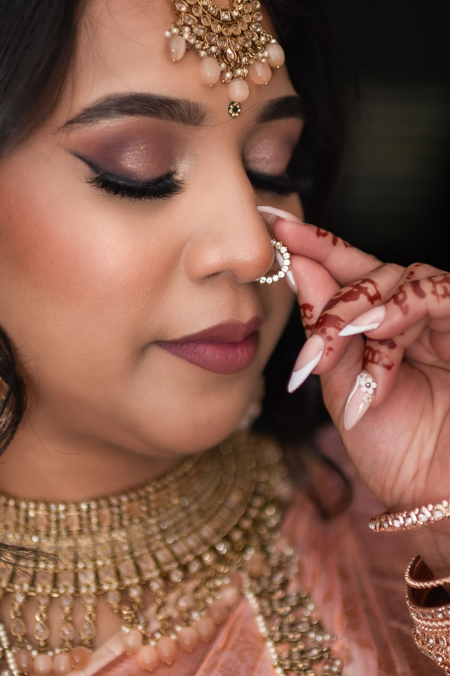 Close-up detail of South Asian bridal makeup and jewelry with ornate gold accessories.