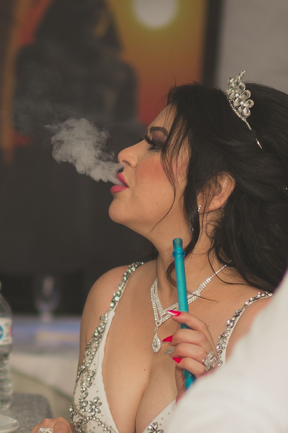 Person wearing sparkly jewelry and formal attire exhales smoke while posing in an artistic portrait series.