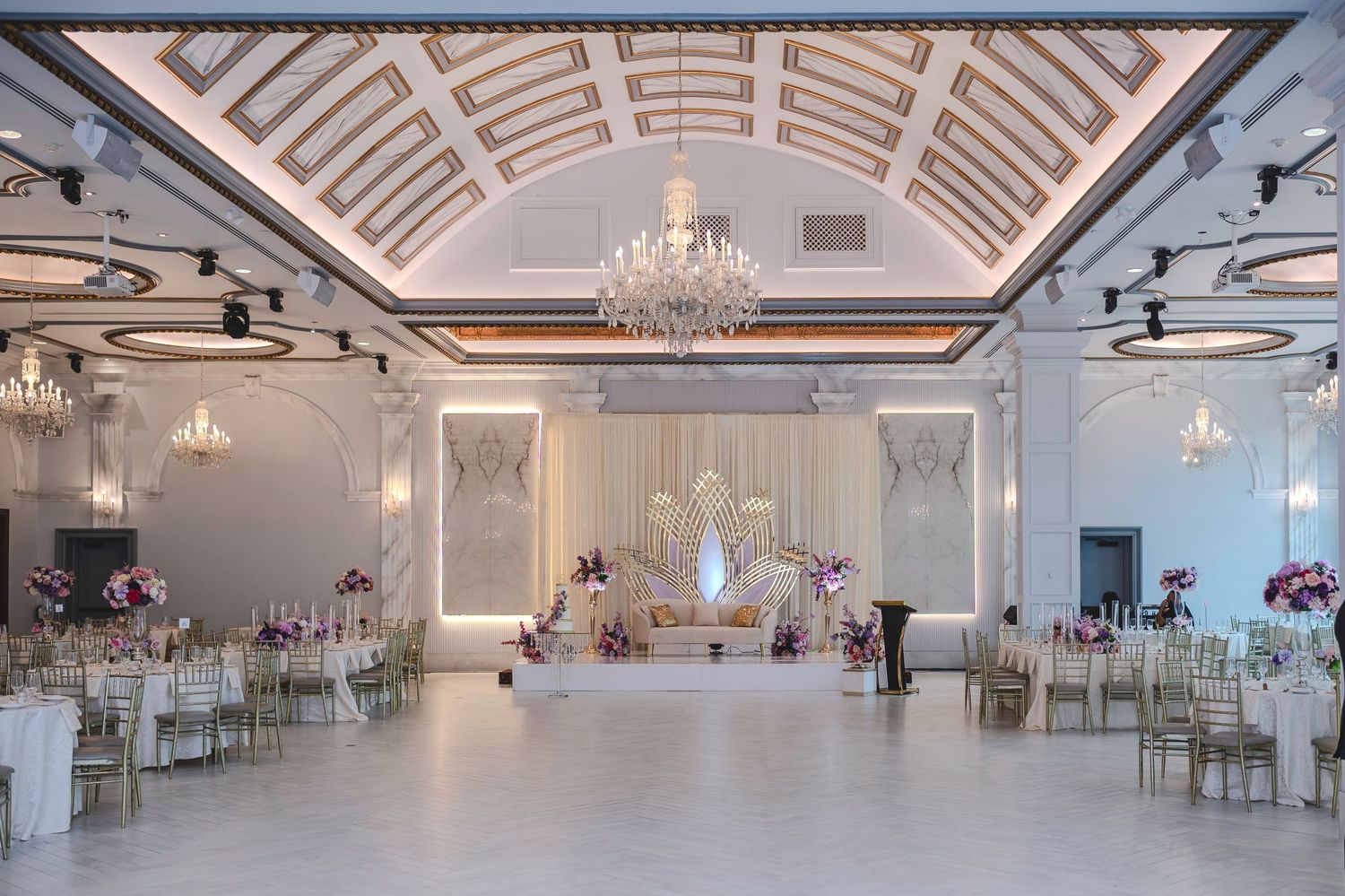 Elegant white ballroom with crystal chandeliers and chiavari chairs set up for a wedding reception.