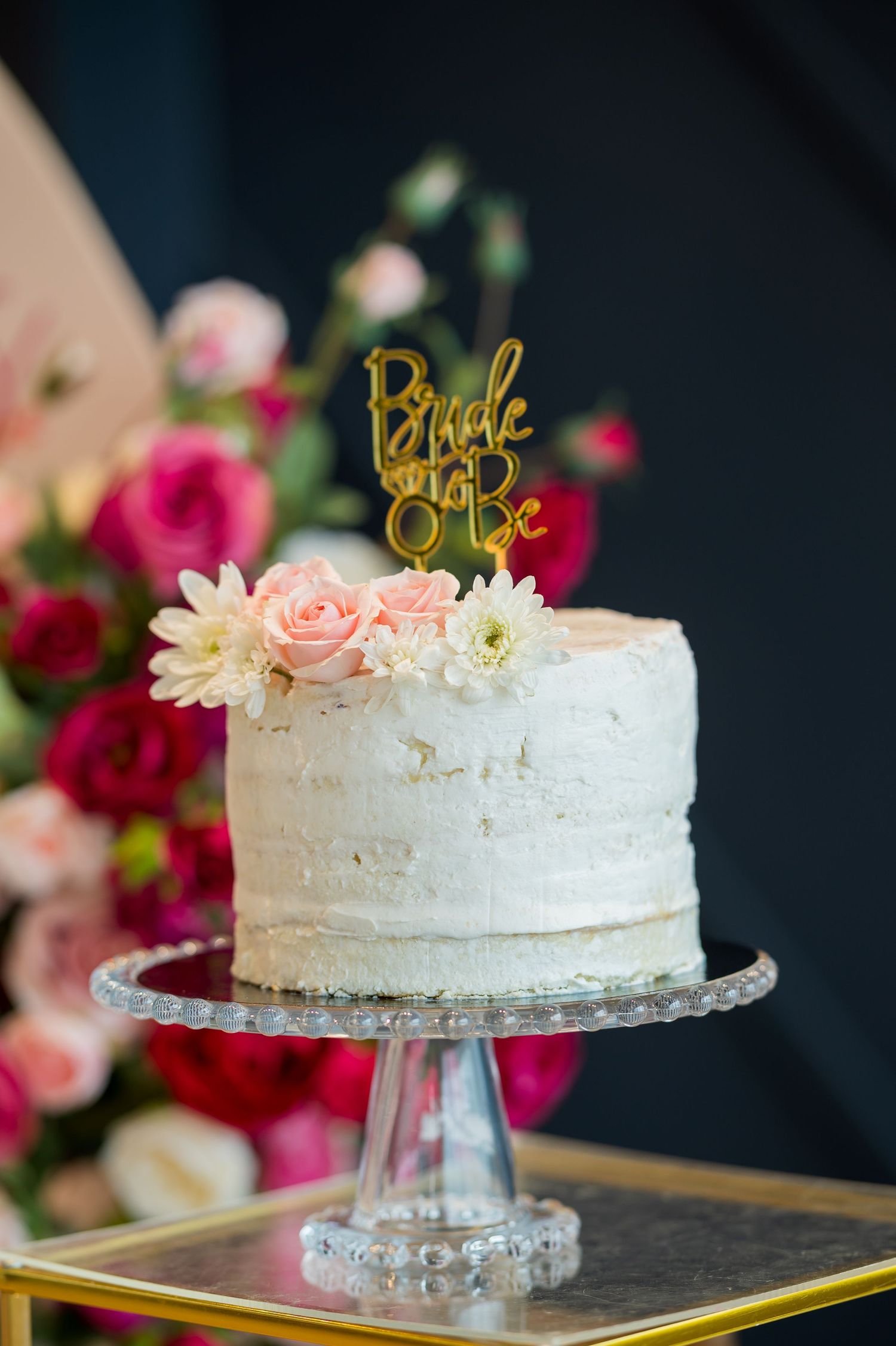 White buttercream wedding cakes with gold toppers and fresh flower decorations.