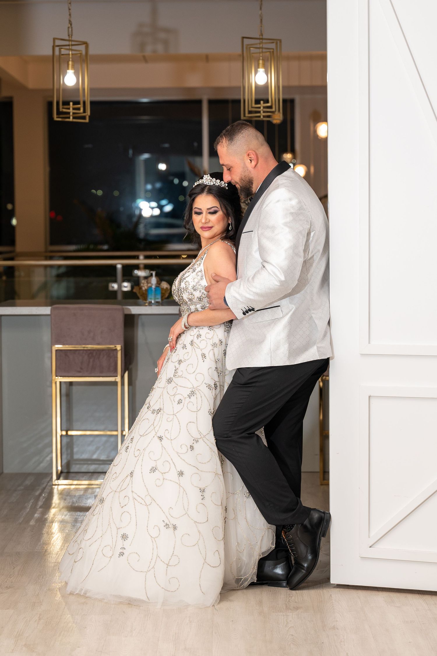 A couple poses elegantly in a modern venue with gold geometric light fixtures.