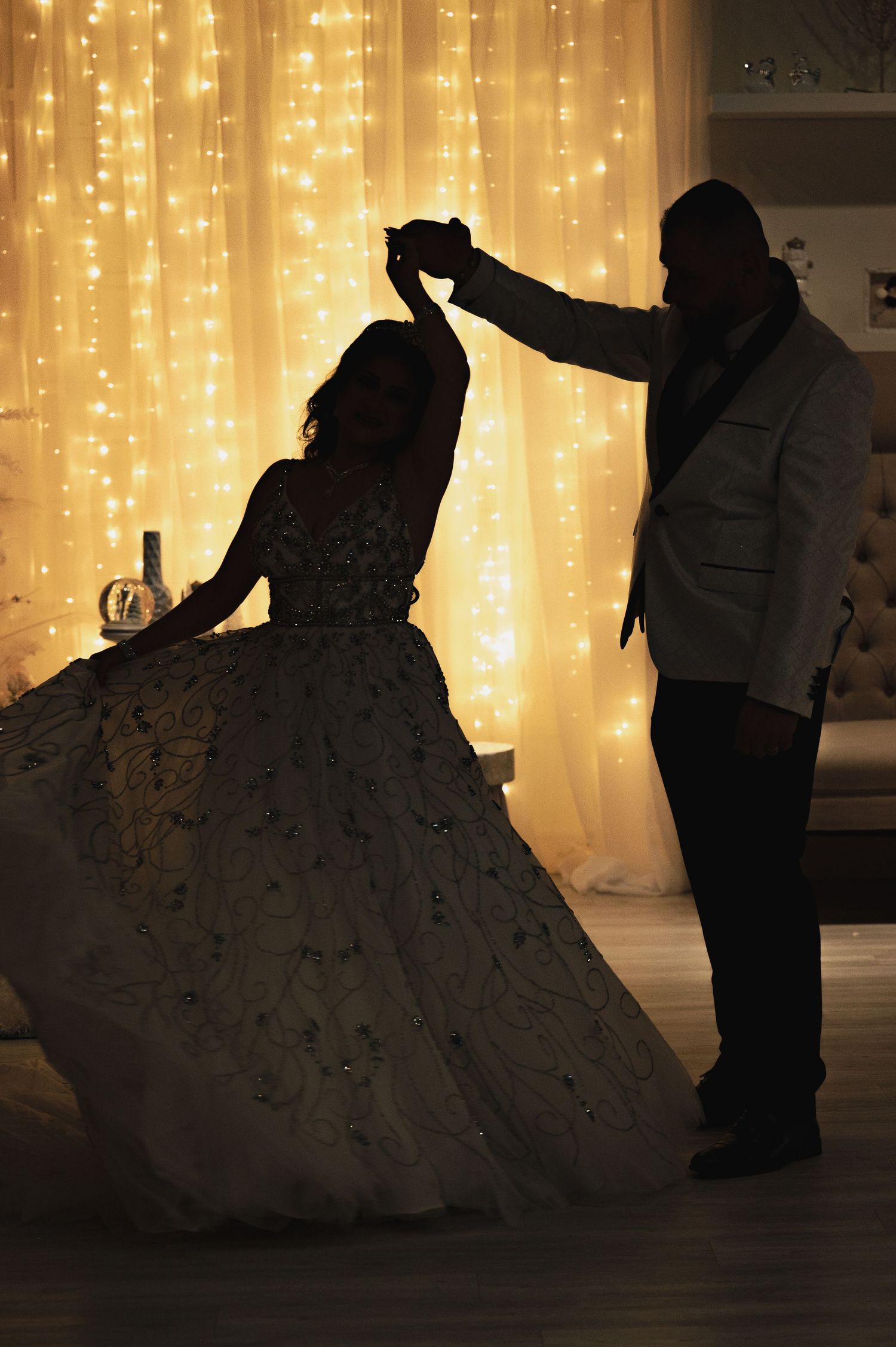 Silhouettes of dancing couples against a glowing backdrop of warm fairy lights create a romantic ballroom atmosphere.