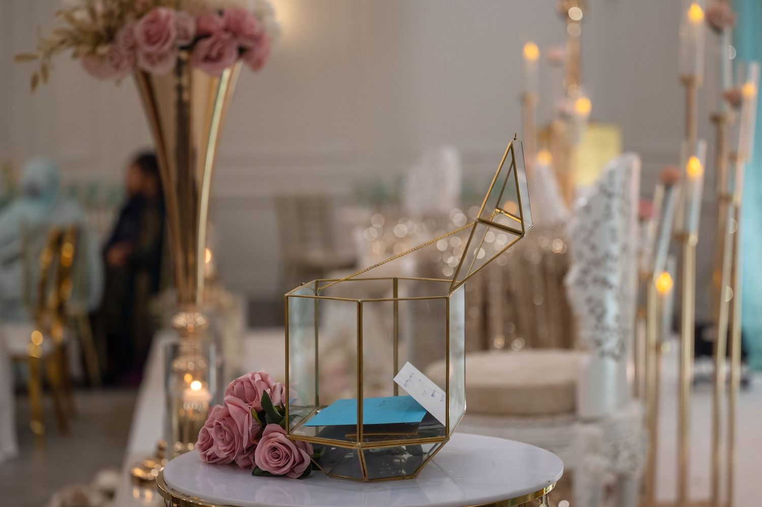 Wedding reception decor with pink roses and golden candle holders on white tablecloth.