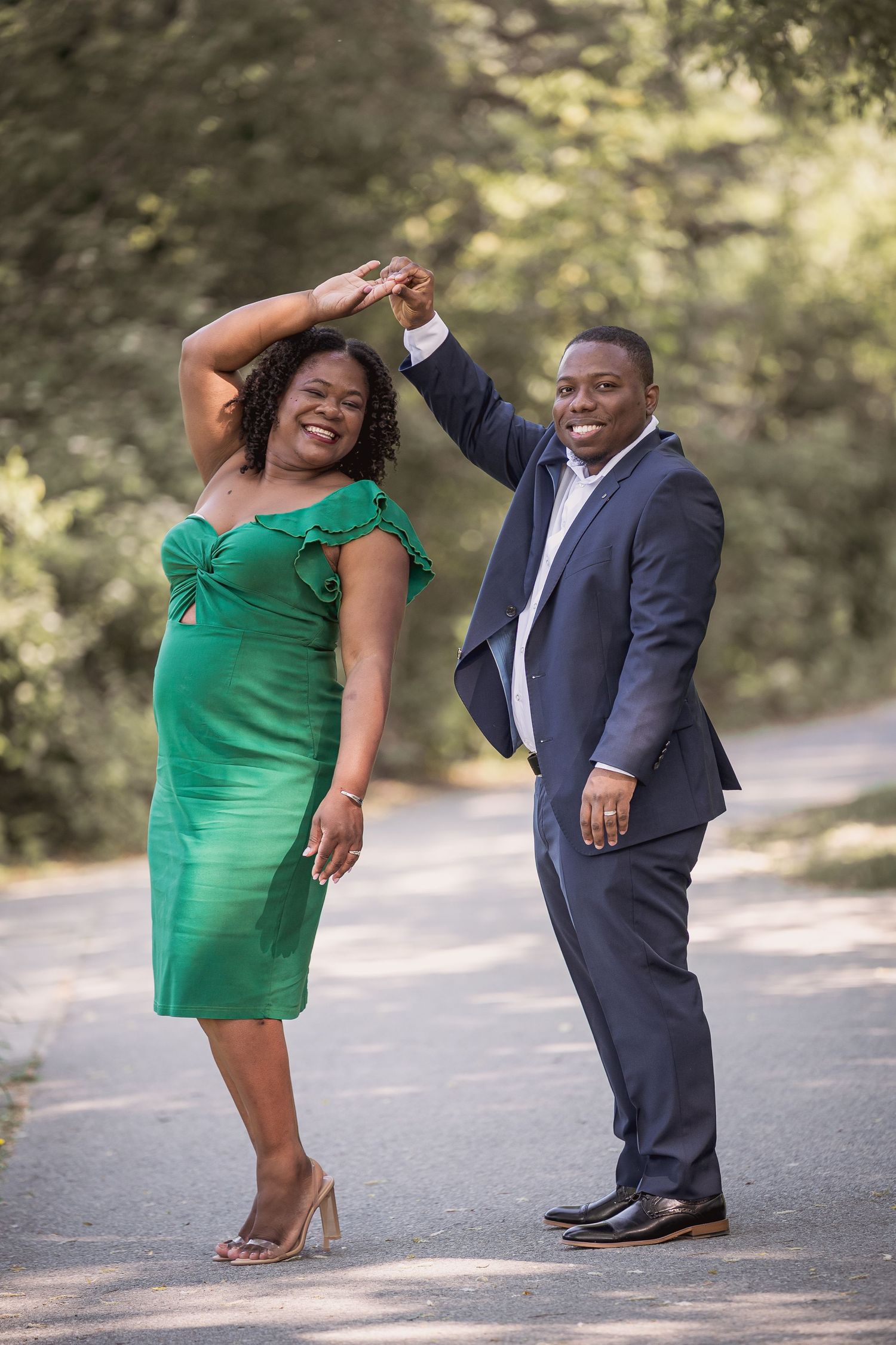 Playful couple in green dress and navy suit dancing during their outdoor engagement session.
