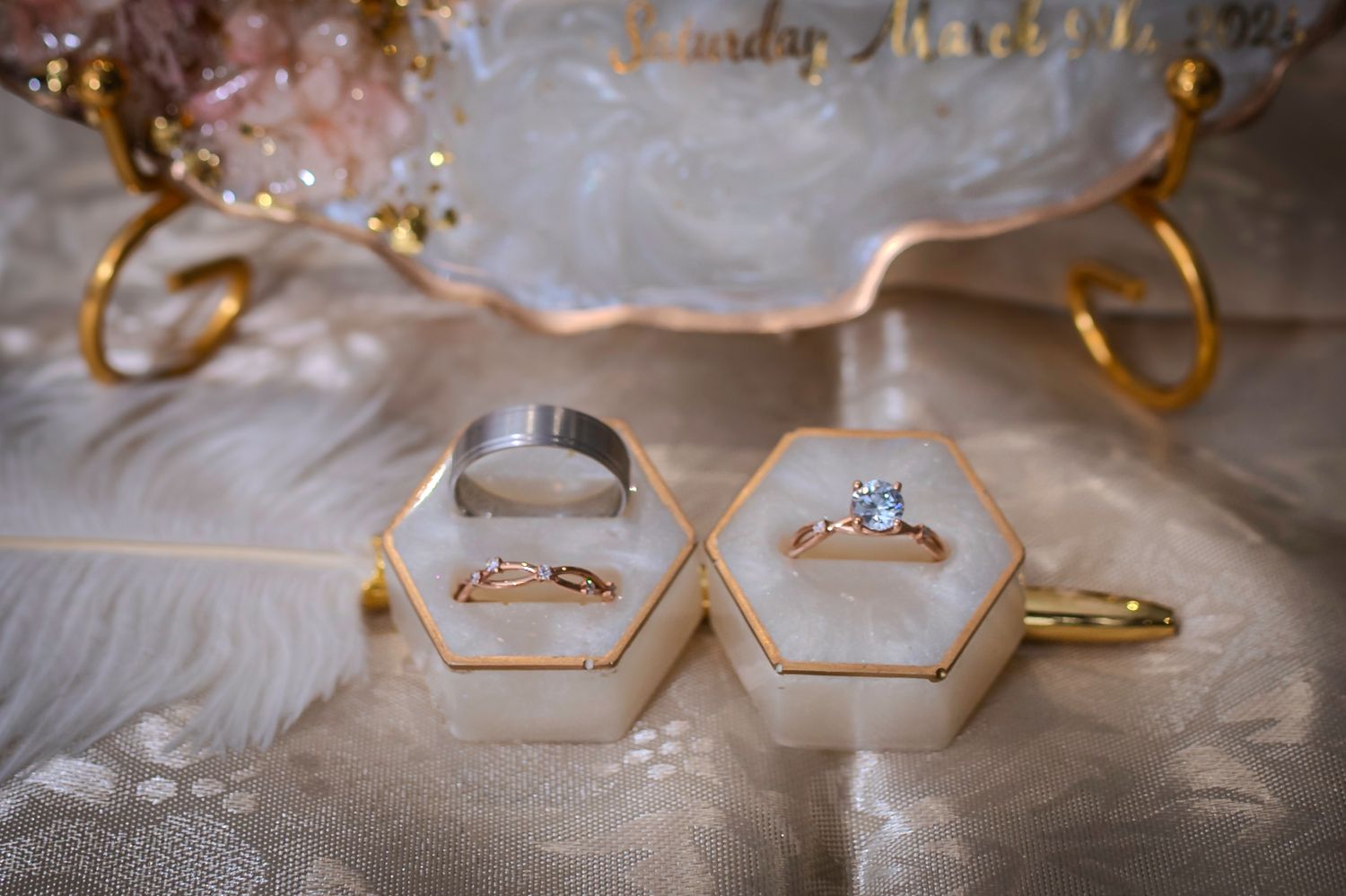 Wedding rings displayed in geometric white ring holders with gold accents.