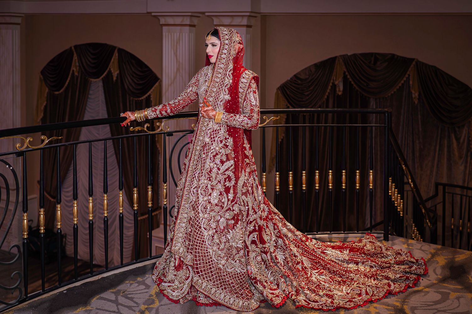 Traditional wedding attire with red and gold embroidered dress near elegant staircase.