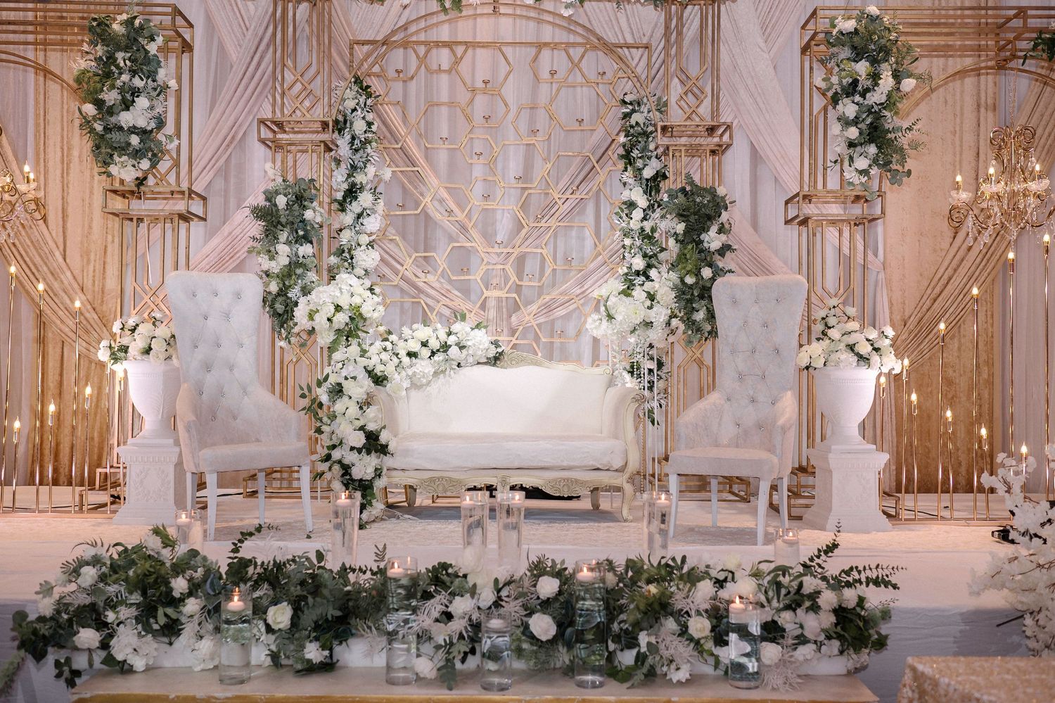 Luxurious white wedding backdrop with ornate panels and cascading floral arrangements.