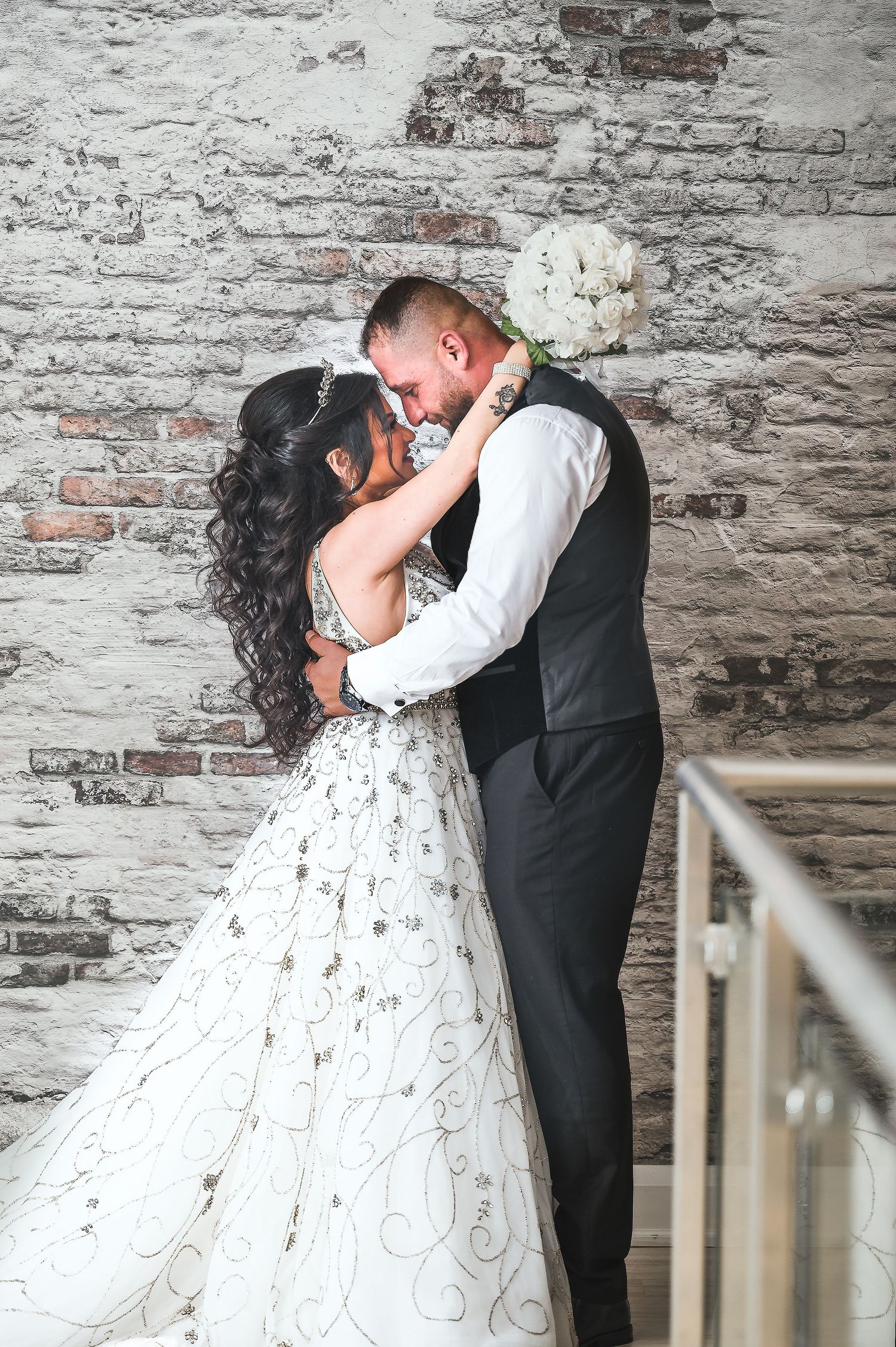Romantic wedding couple embracing against a rustic brick wall backdrop.