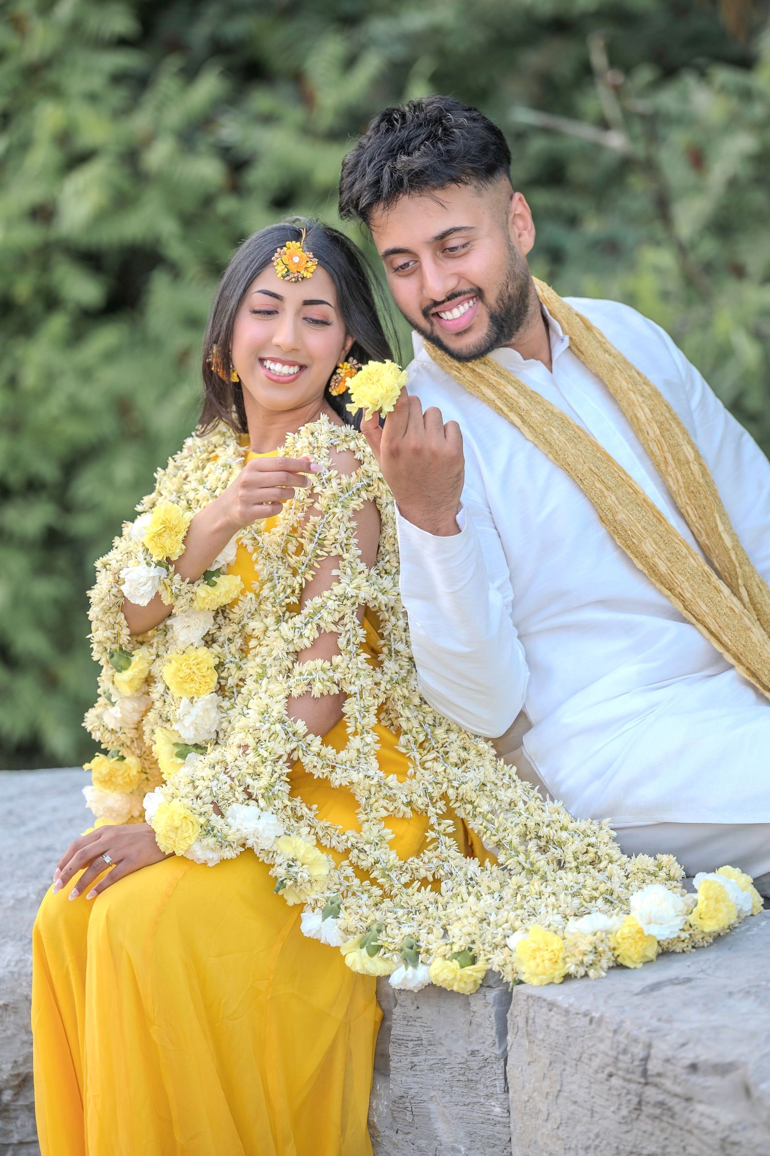 Candid moments captured on stone wall featuring yellow dress adorned with delicate white flowers.