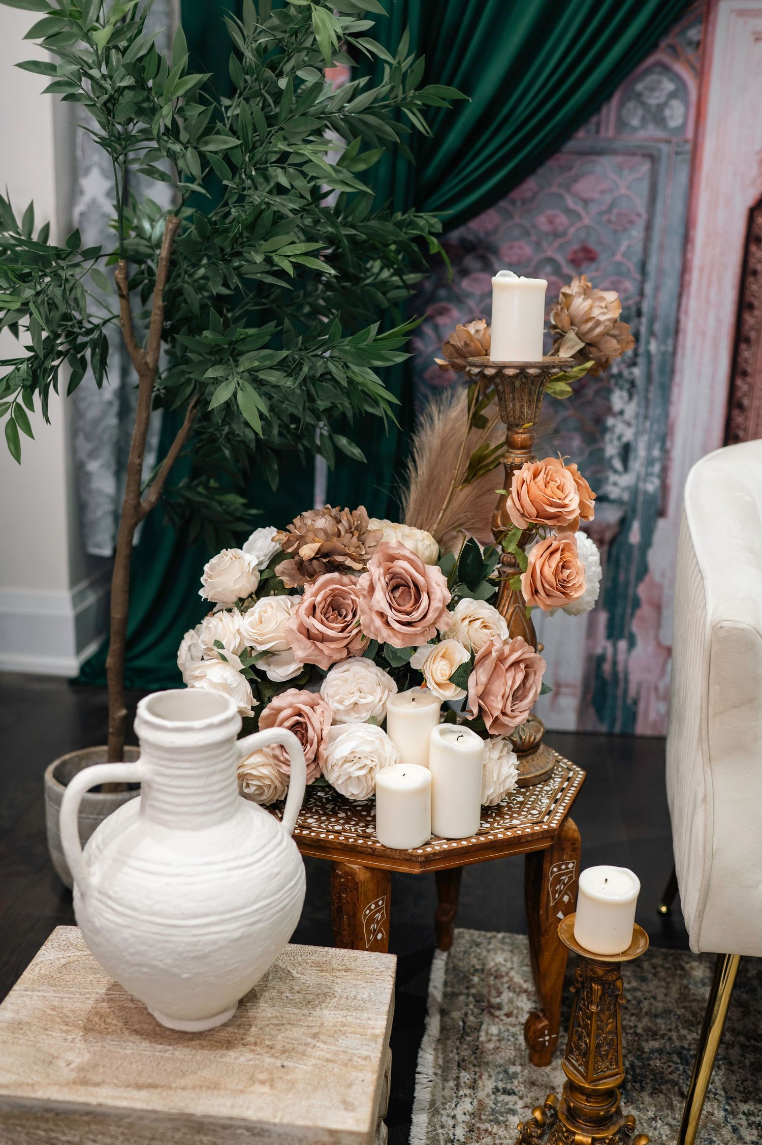 Wedding decor featuring white ceramic vases, candles, and peach roses against green drapery.