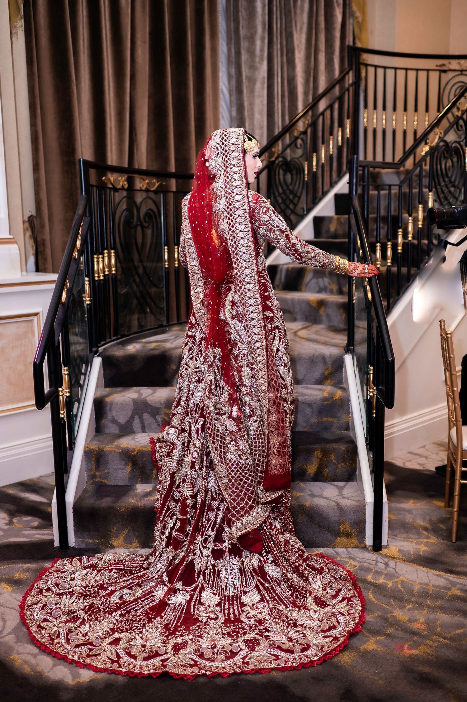 Intricate red and gold embroidered wedding dress train displayed on marble floor.