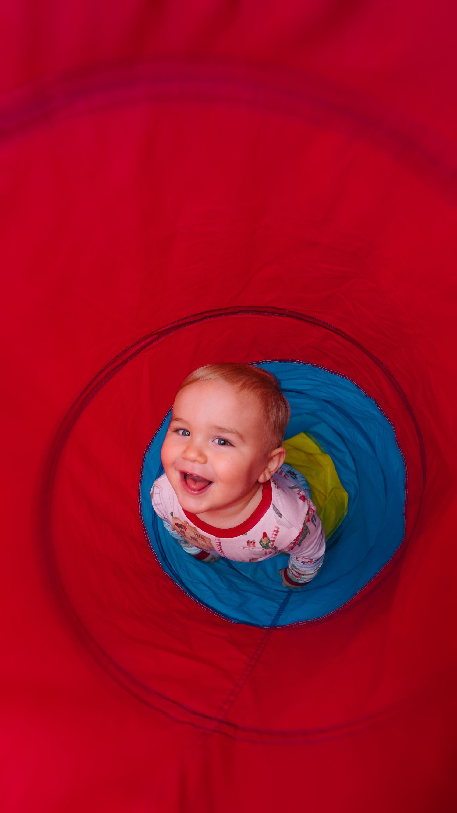 Baby peeking through circular opening in red blanket during creative photo shoot.