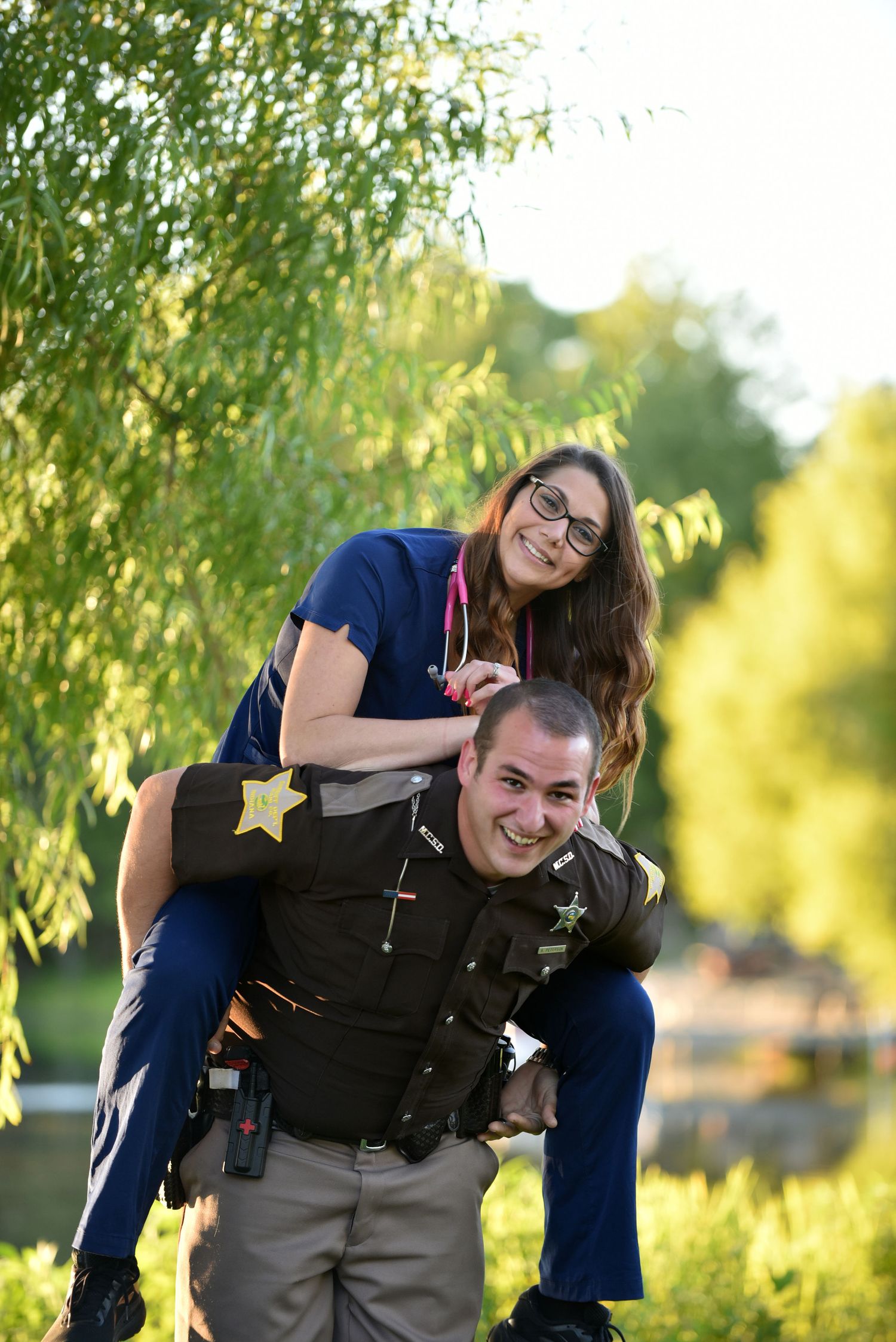 Playful couple with law enforcement uniform having fun outdoors near a lake on a sunny day.