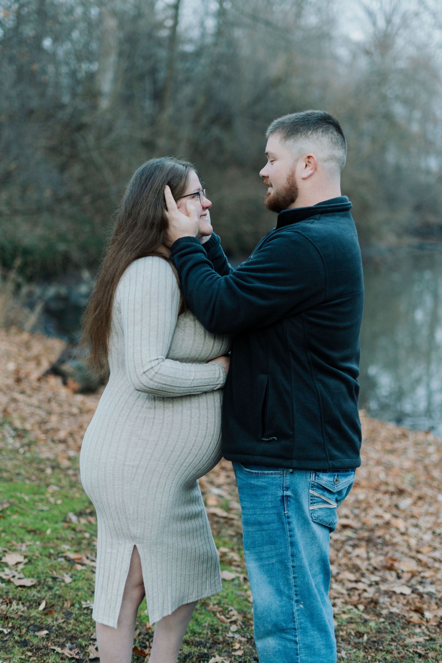 Romantic maternity photos of couple in casual wear against autumn forest backdrop.