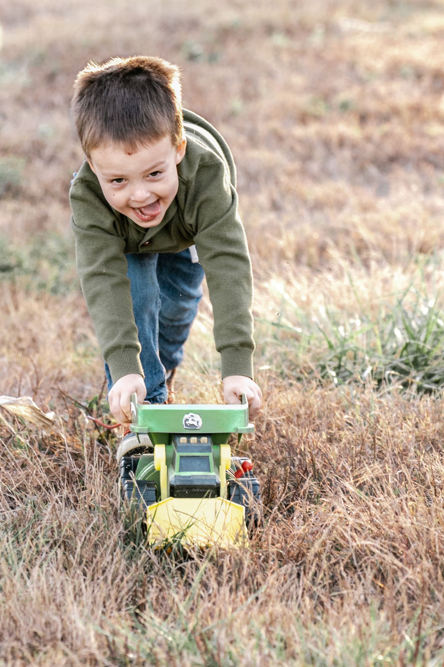 Young child playing with a toy truck in dry grass during fall season.