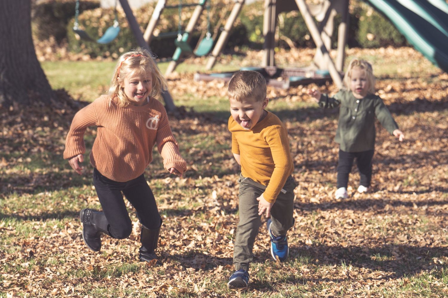 Children playing near playground equipment on a sunny autumn day.