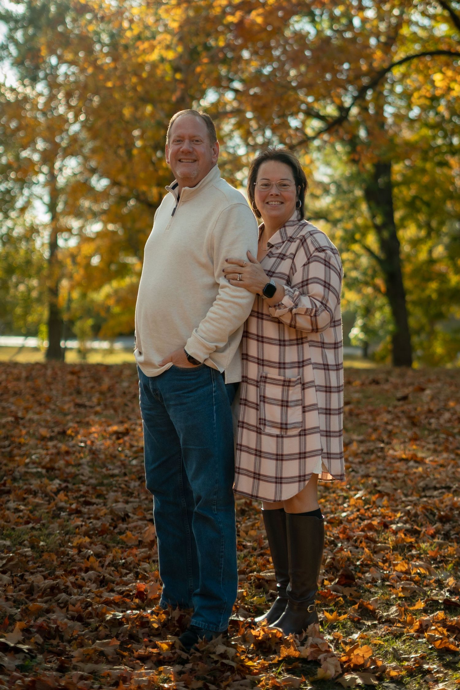 Two people embrace while standing among colorful fall foliage.
